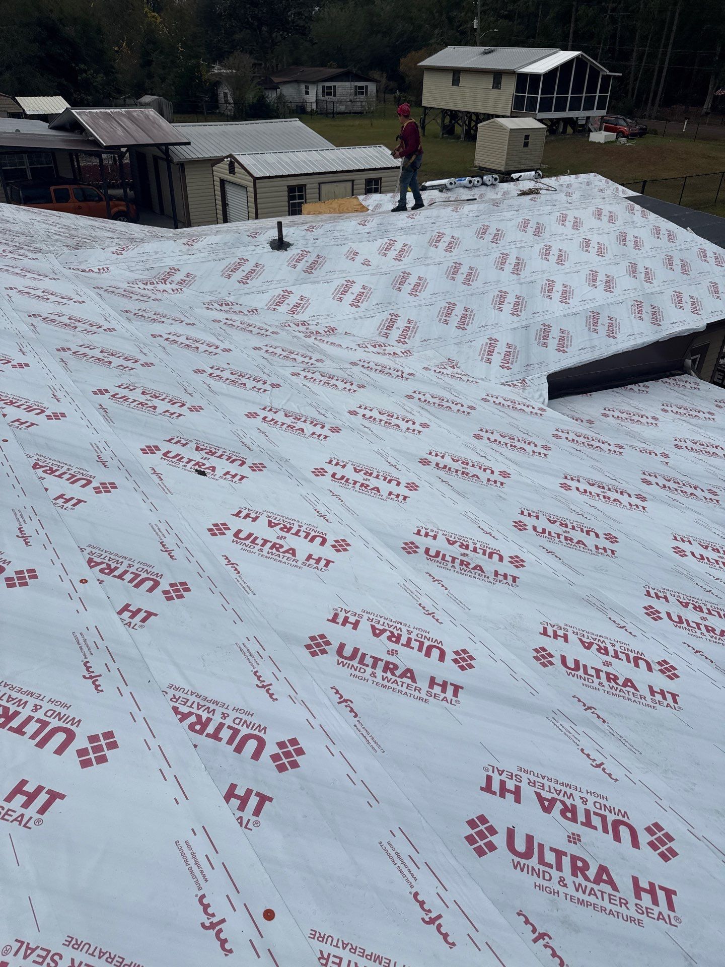 Roofer standing on a roof covered in white underlayment, preparing for new roofing. Buildings are in the background.