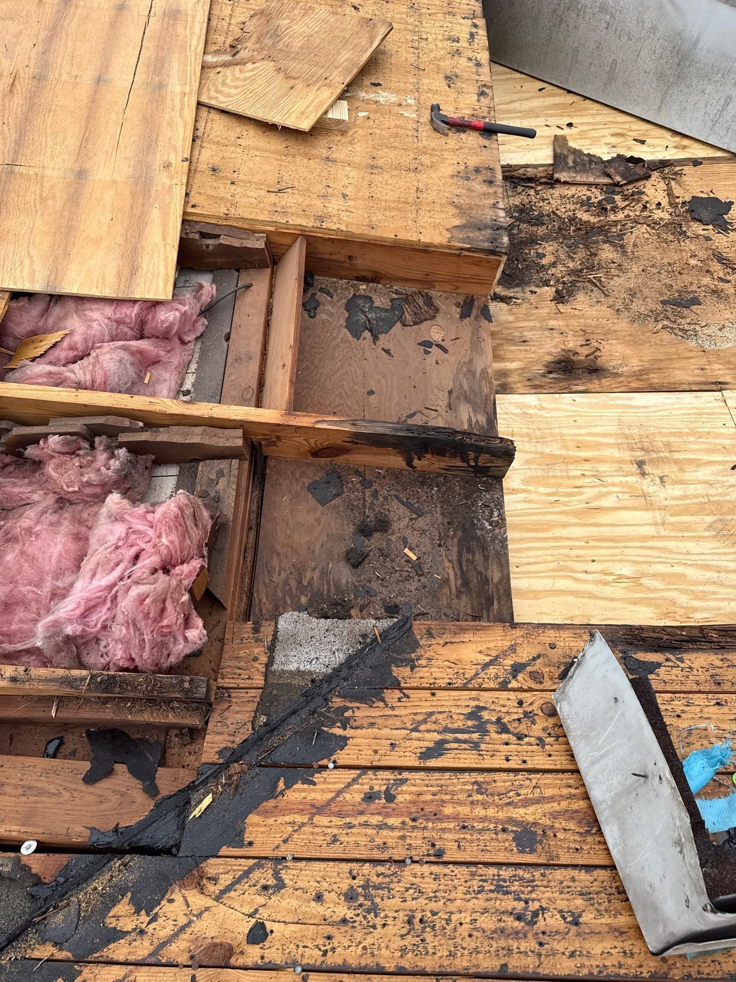Damaged roof section with exposed wood, insulation, and black sealant.