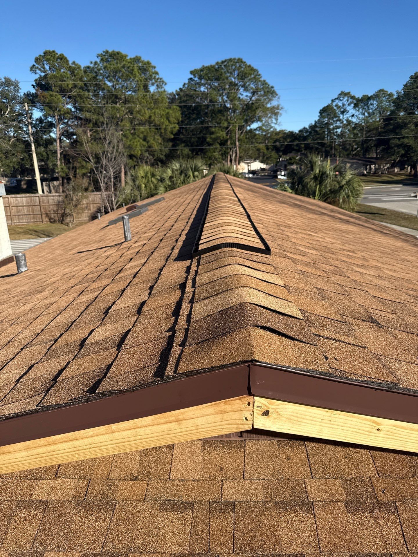 Brown shingle roof with a ridge vent. Brown trim and a clear blue sky.
