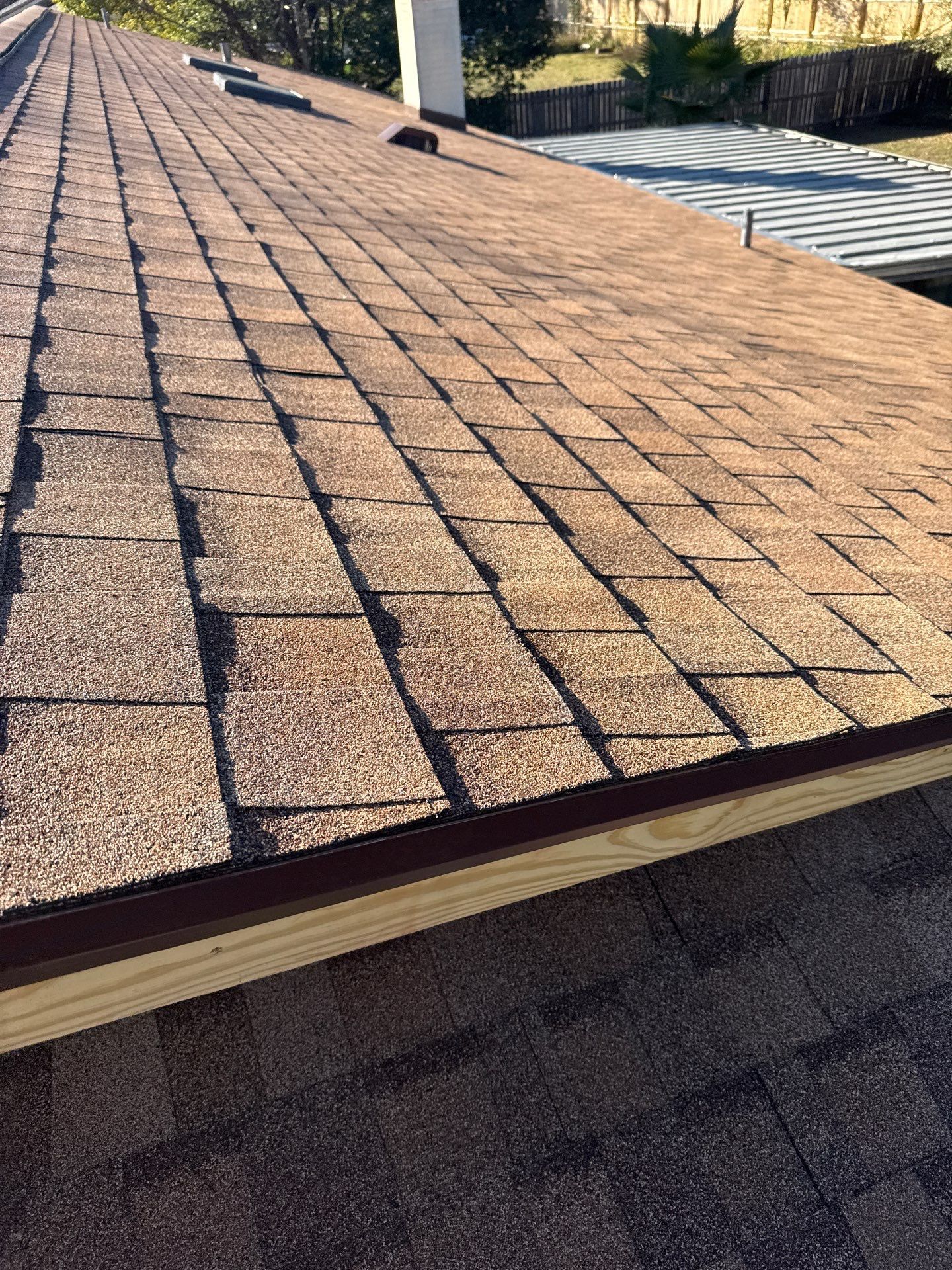 Brown asphalt shingle roof. View from above, showing texture, wooden trim, and shadow patterns.