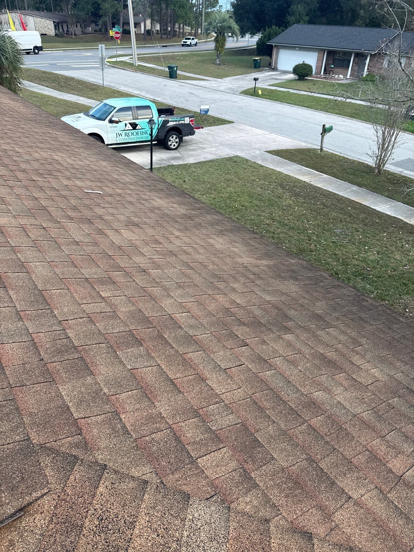 Brown roof with shingles, a teal pickup truck in the driveway, and a suburban street.
