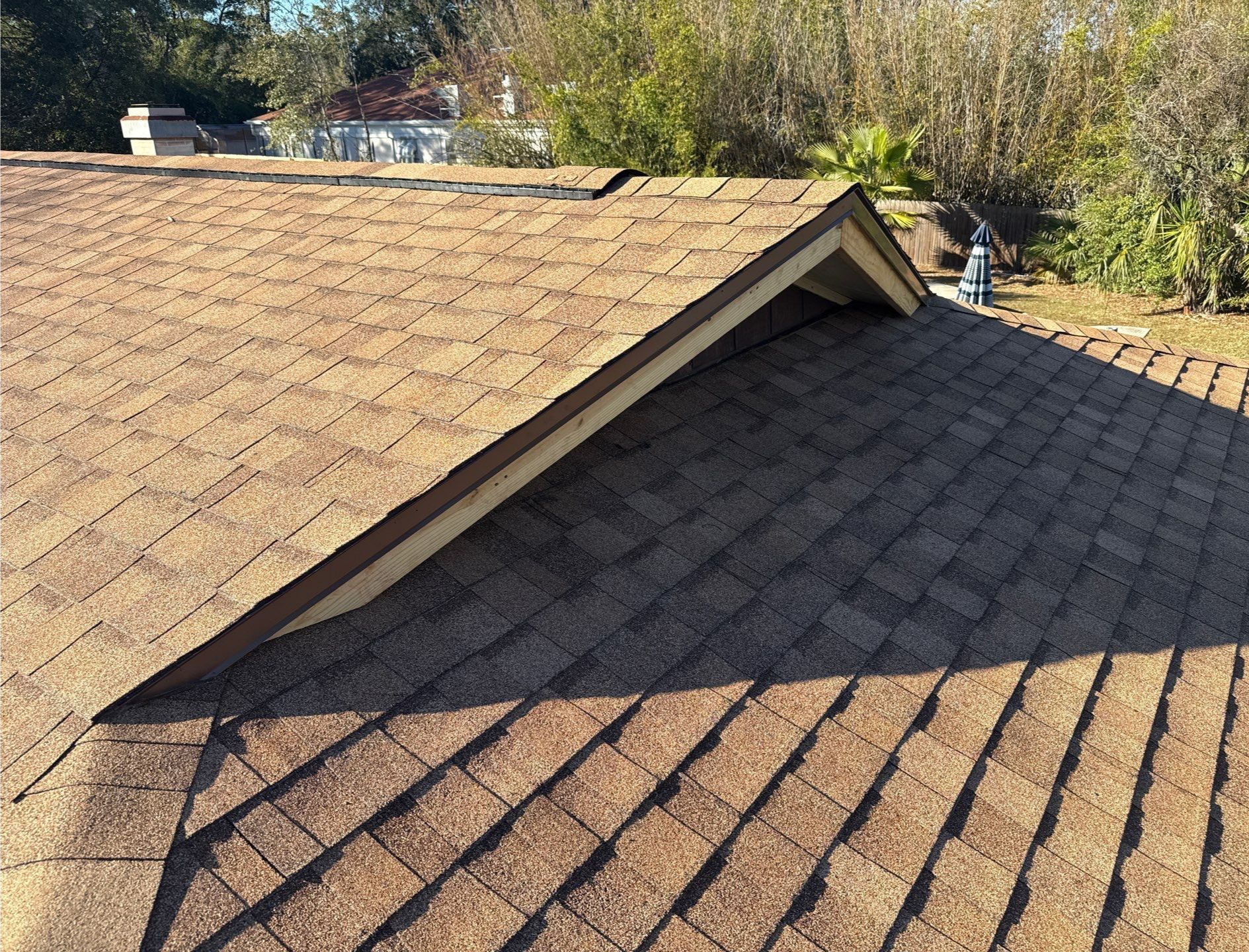 Brown shingled roof with a small triangular gable. Daylight with shadows.