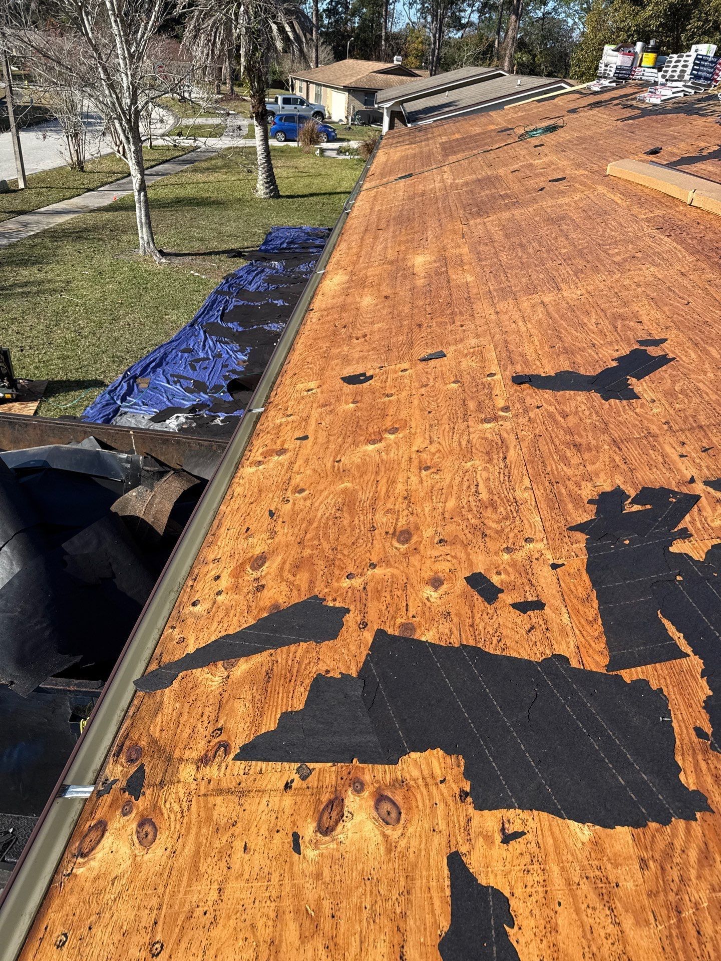 Roof with removed shingles, showing exposed wood and a blue tarp.