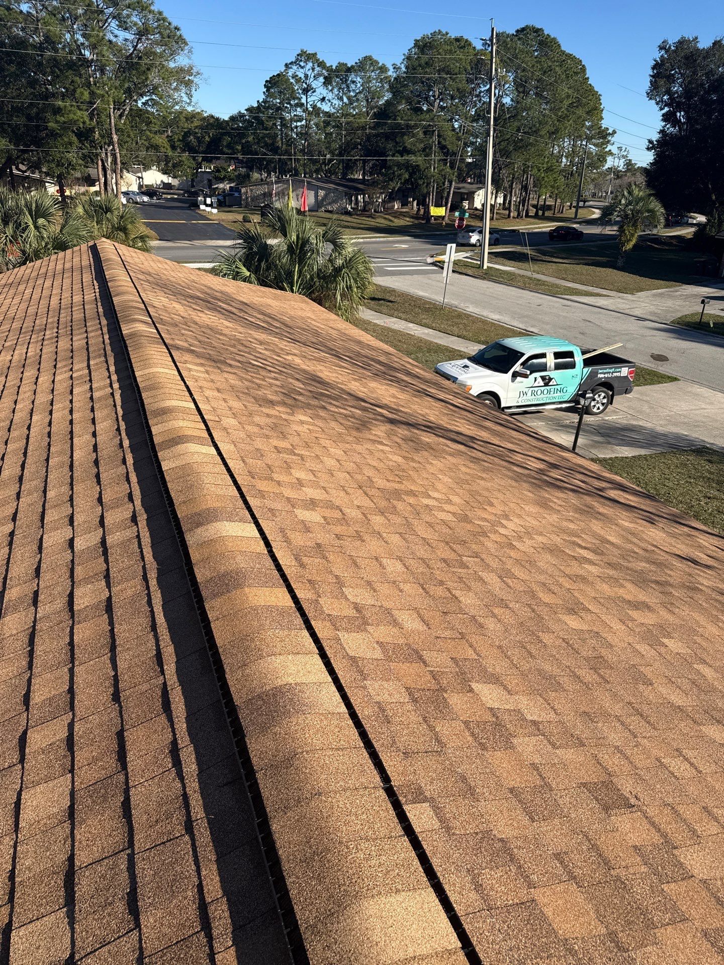 Brown shingled roof with a truck on the street below; clear sunny day.