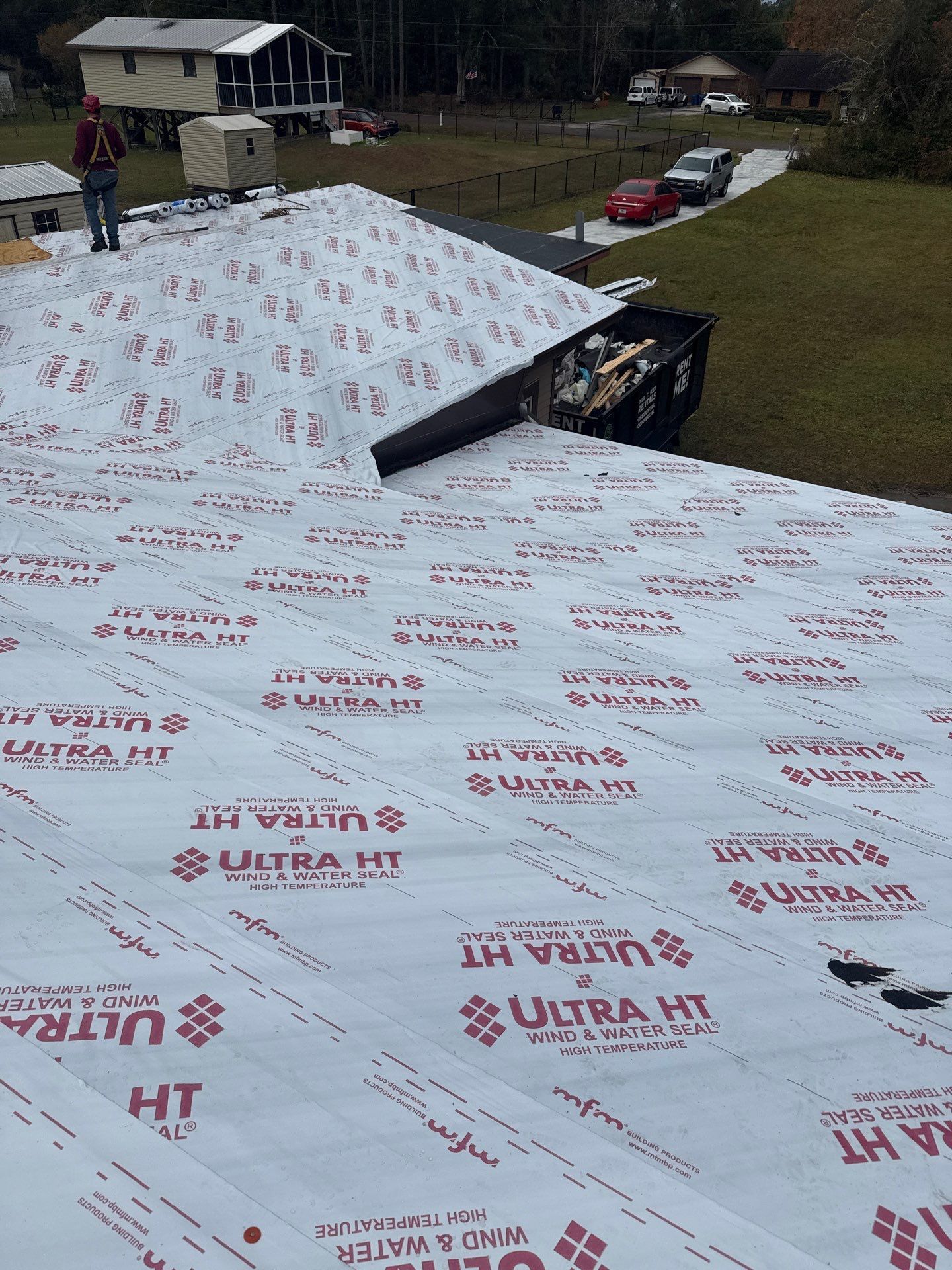 Roofer on a house roof covered in white underlayment, tools in a container.