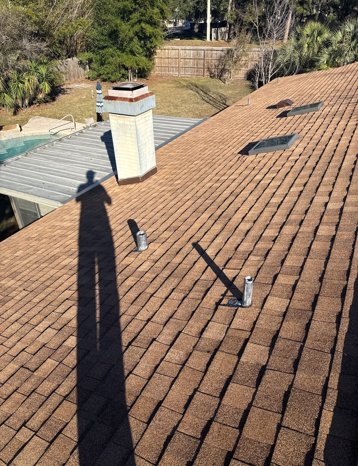 Shadow on a brown shingle roof with chimney and skylights.