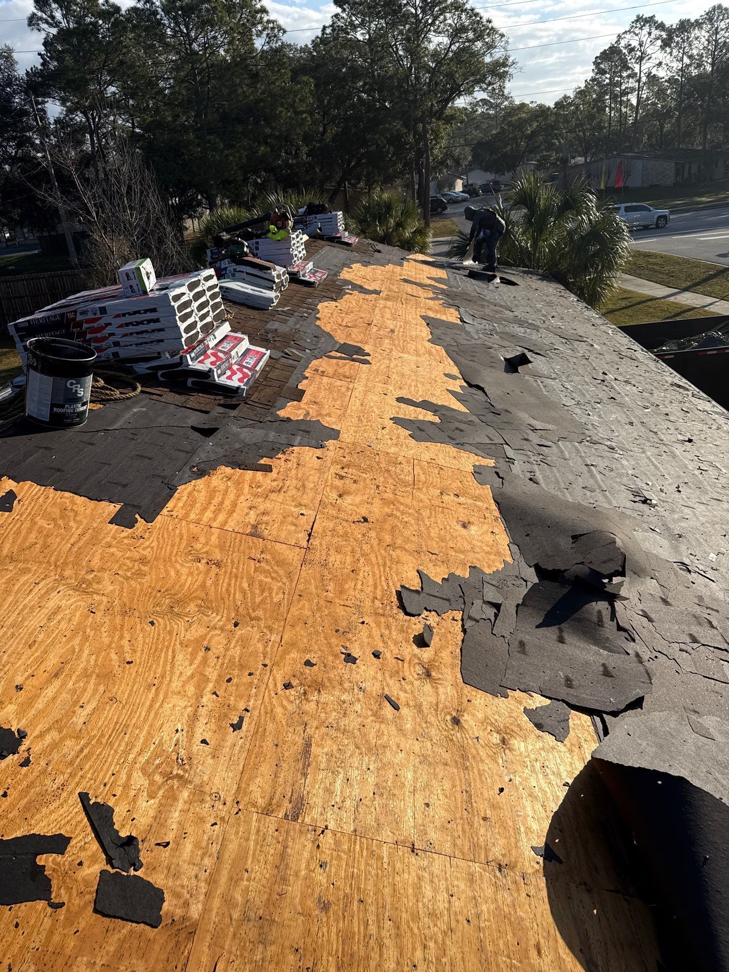Roof partially stripped of shingles, showing plywood underlayment, and materials.