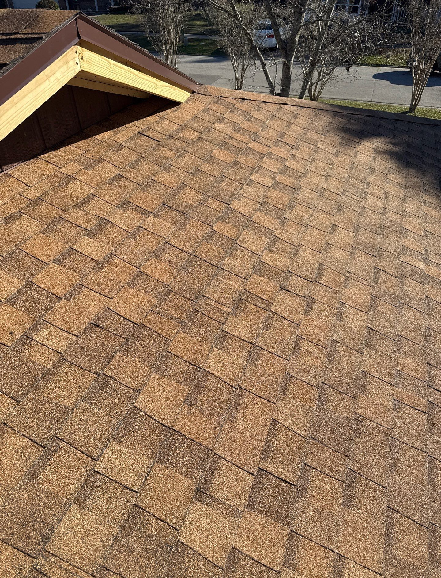 Close-up of brown shingle roof with a wood-framed edge, angled with the road visible in the background.