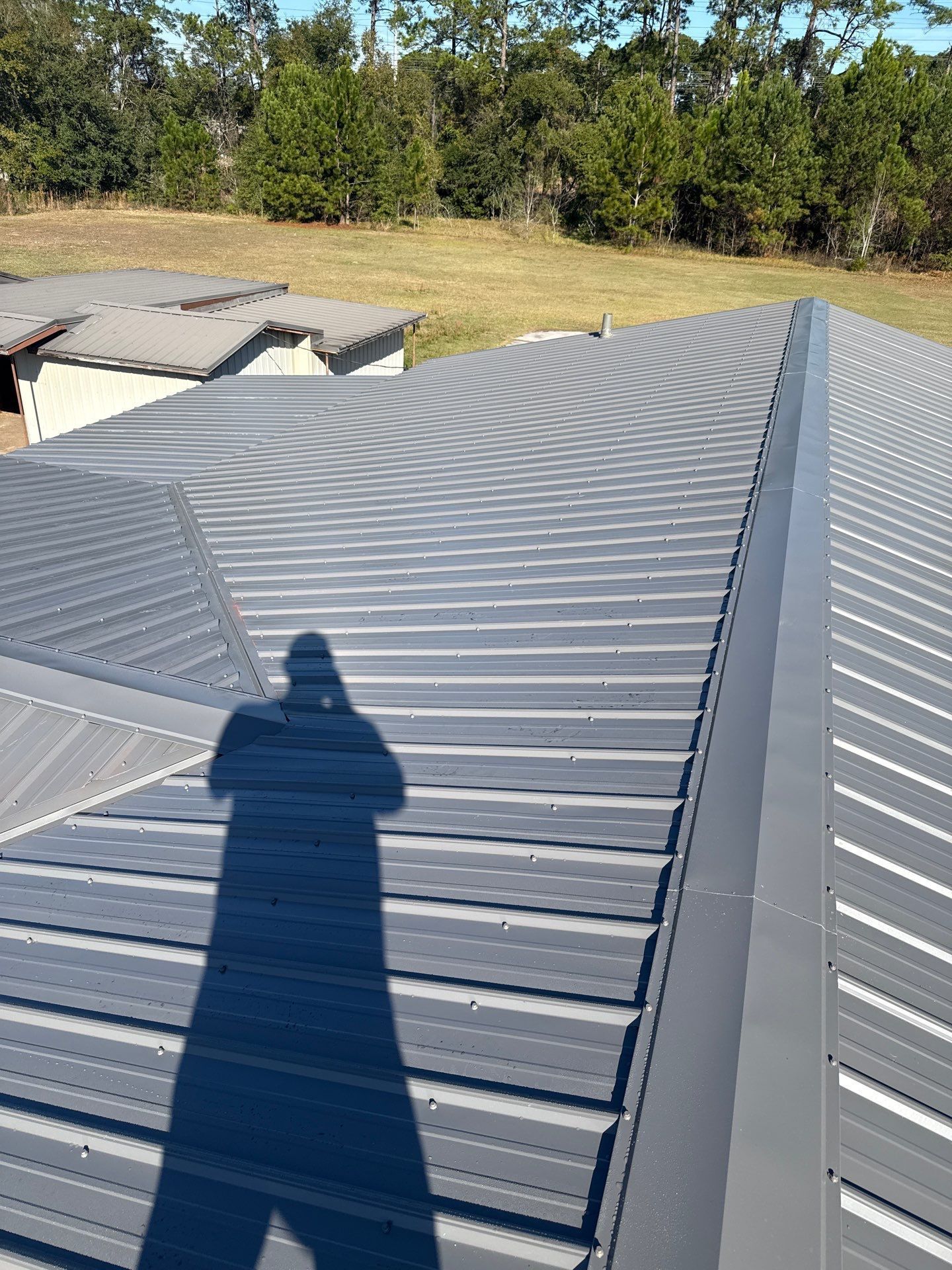 Shadow of a person on a gray metal roof, with trees and a building in the background.