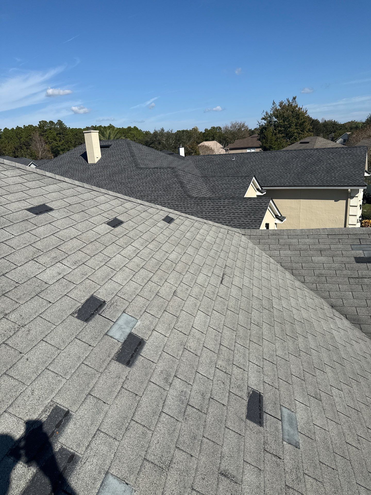 Close-up of a roof corner with black and gray asphalt shingles and dark trim, under construction.