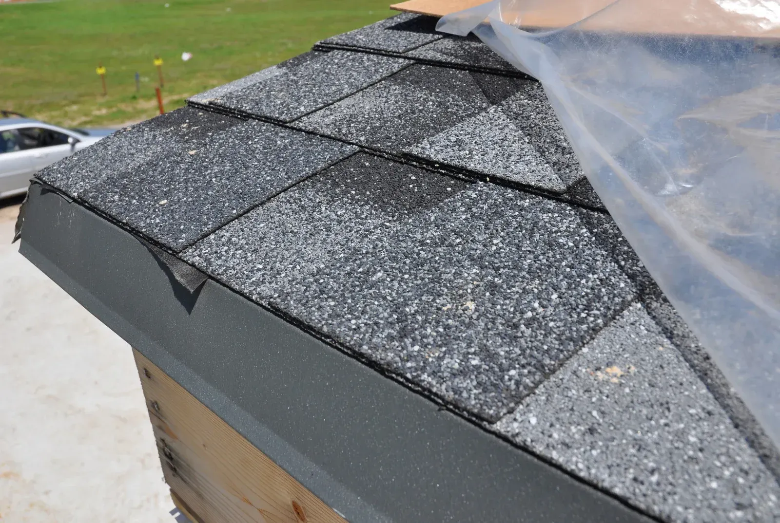 Close-up of a roof corner with black and gray asphalt shingles and dark trim, under construction.