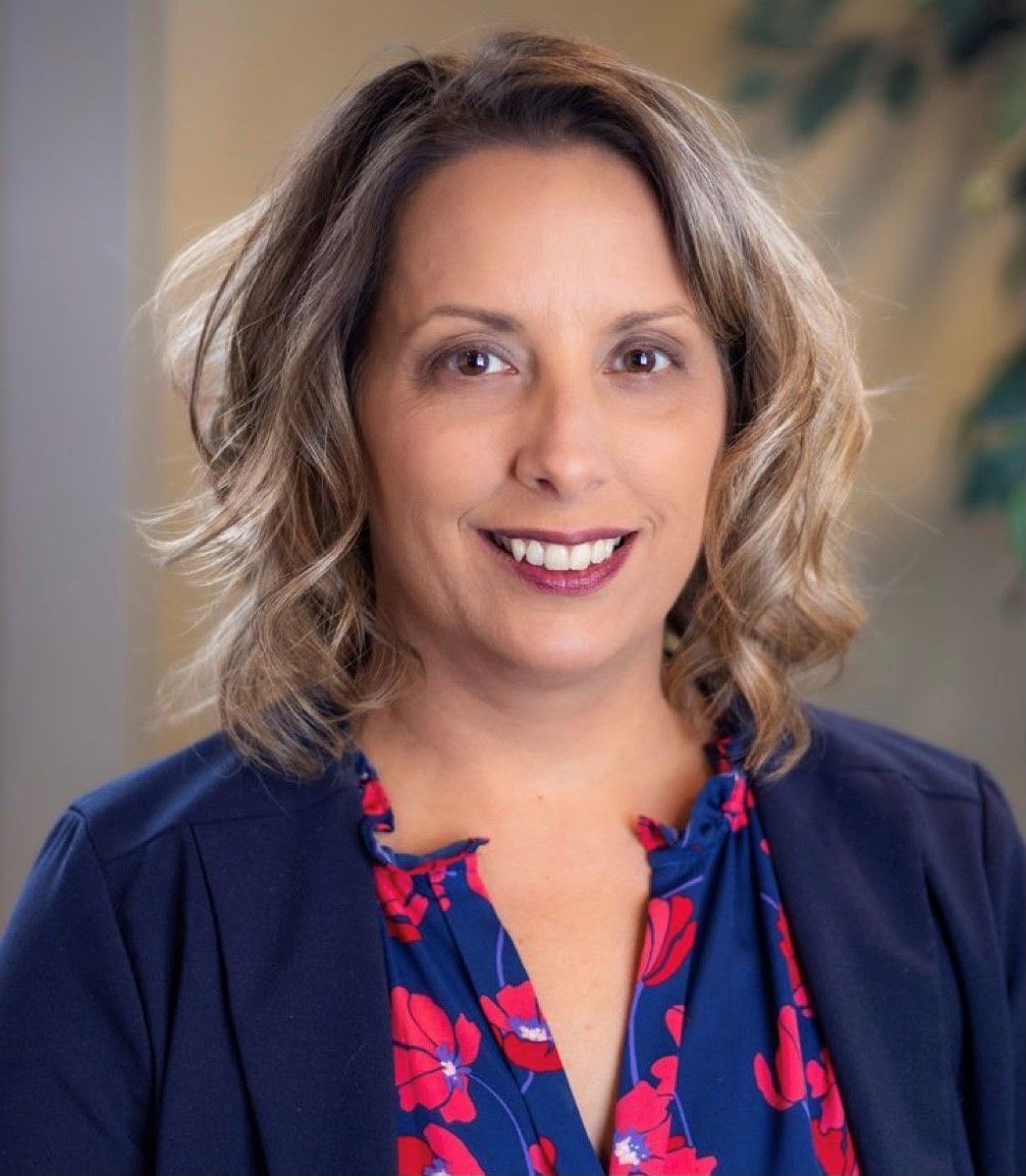 Woman with brown hair smiles, wearing a blue blazer over a floral top. Woman with brown hair smiles, wearing a blue blazer over a floral top.