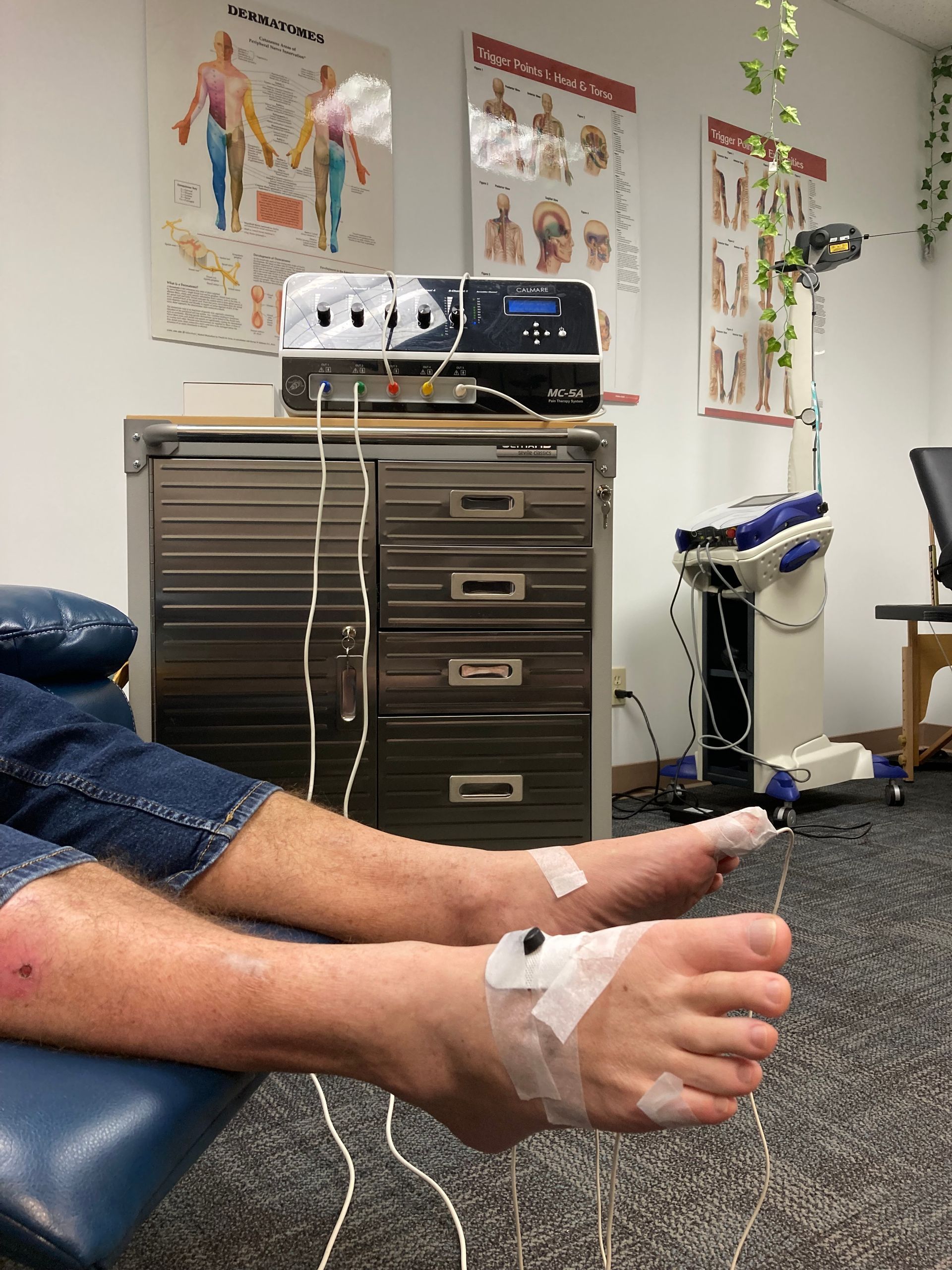 Person's feet connected to medical equipment in a clinic. Wires, electrodes, and a machine are visible. Person's feet connected to medical equipment in a clinic. Wires, electrodes, and a machine are visible.