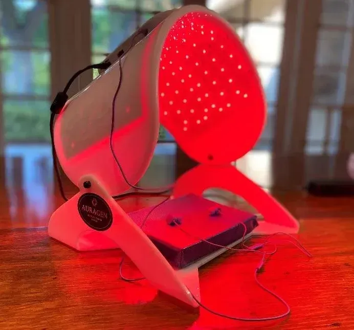 Red light therapy device on a wooden table. White frame with red LED lights, a headband, and attached purple device. Red light therapy device on a wooden table. White frame with red LED lights, a headband, and attached purple device.