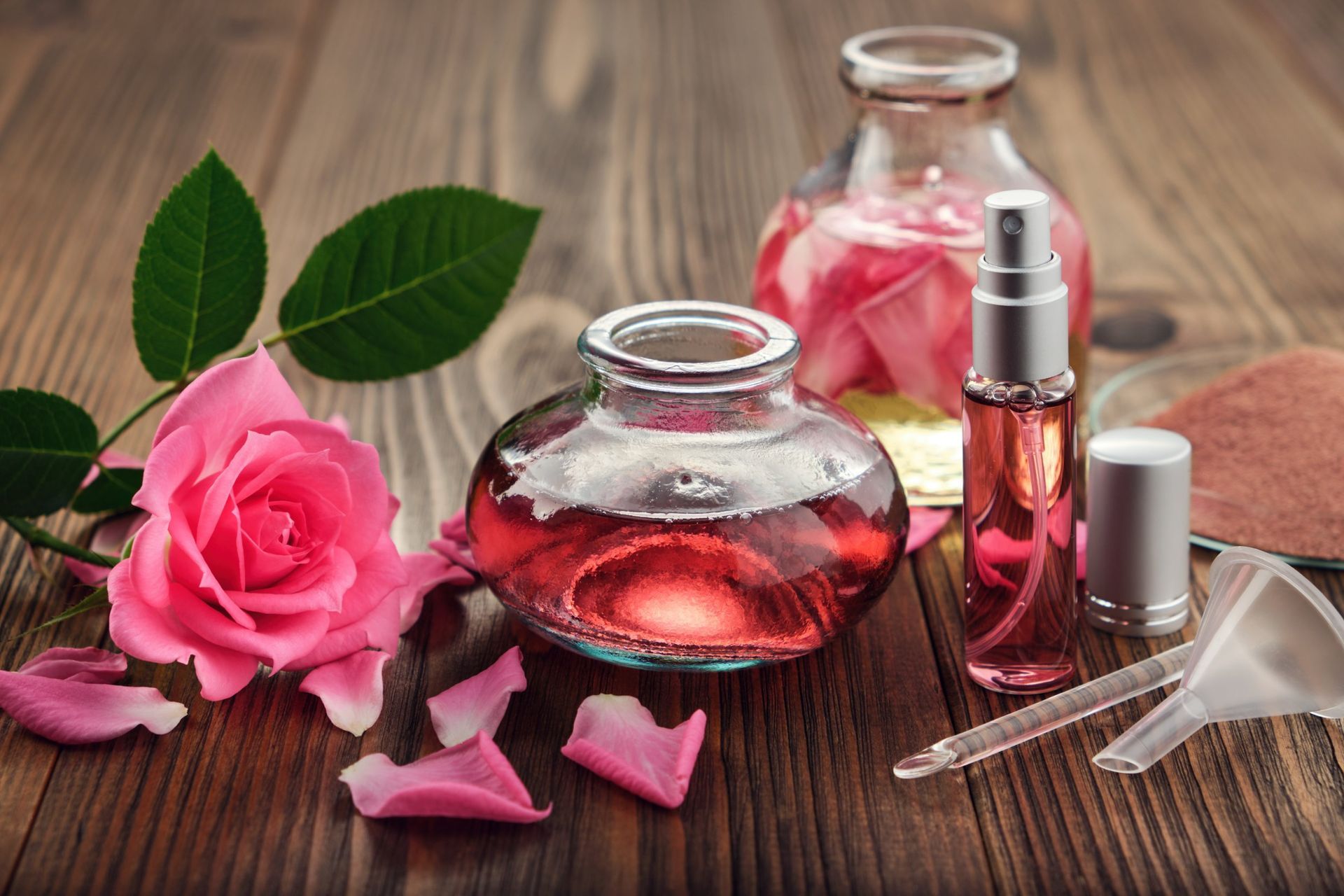 Rose cosmetics and perfume bottles with pink rose petals on a wooden table