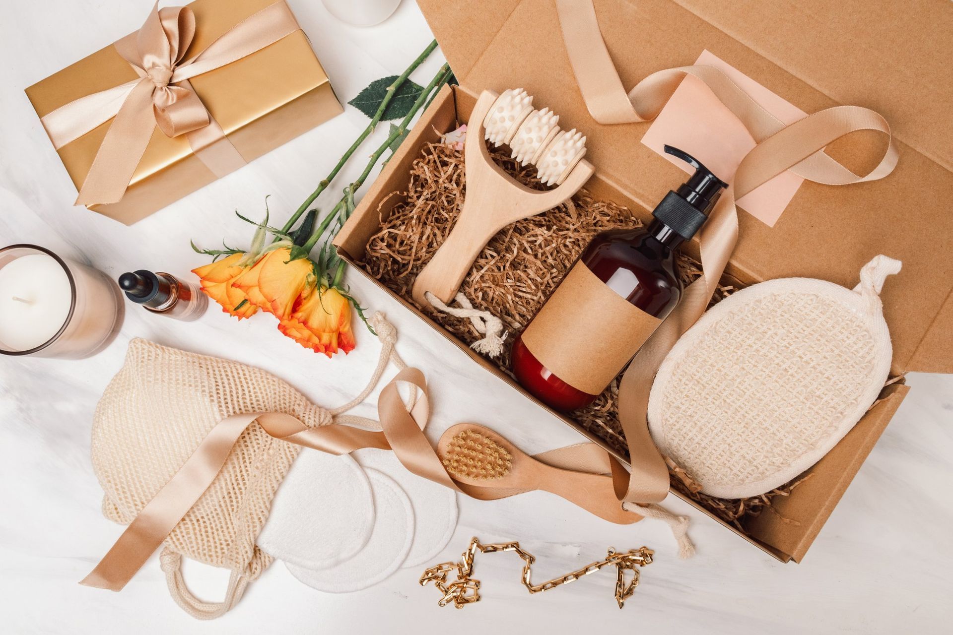 Gift box with ribbon, bottle, flowers, candle, and jewelry on a light background