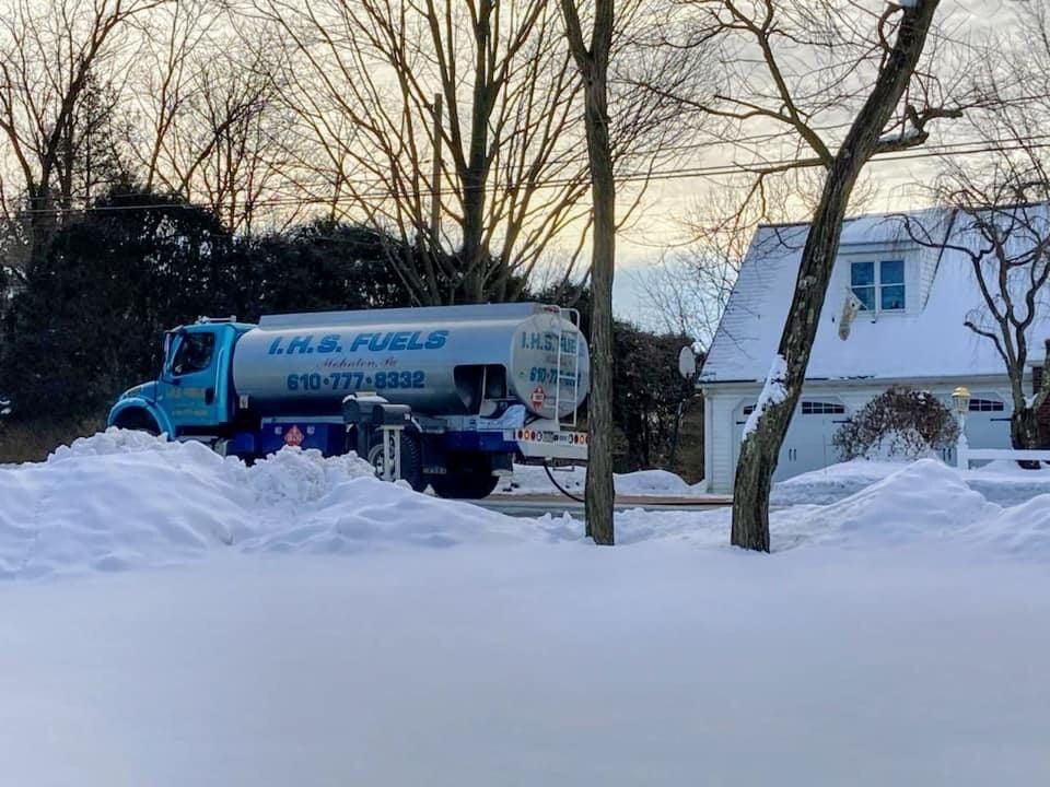 A tanker truck is parked in the snow in front of a house.