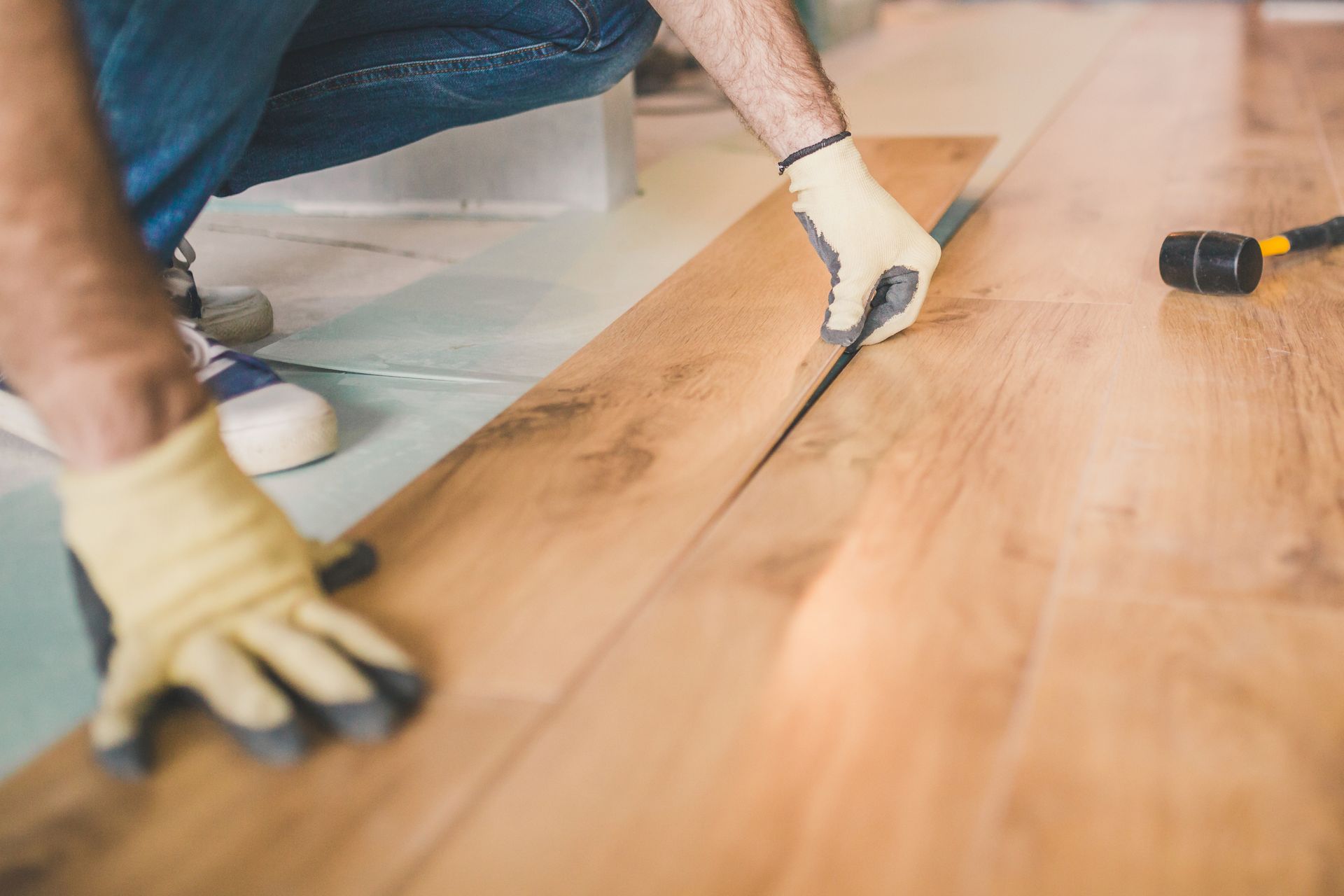 Person installing hardwood flooring with a tool and gloves in a room Person installing hardwood flooring with a tool and gloves in a room