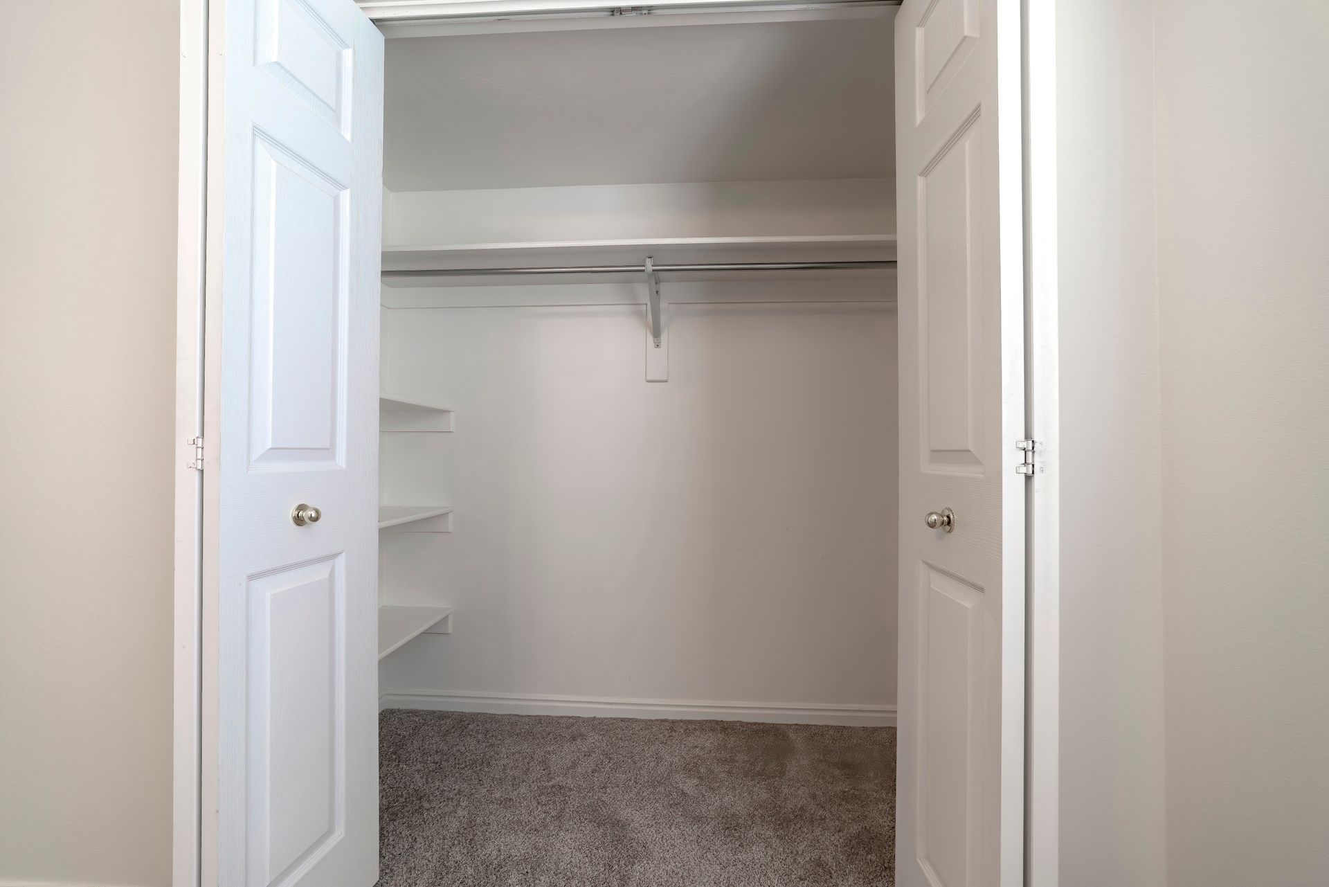 Open closet with white double doors, hanging rod, and carpeted floor Open closet with white double doors, hanging rod, and carpeted floor