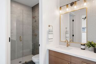 Modern bathroom with glass shower, mosaic tile, and vanity with gold-framed mirror and lights Modern bathroom with glass shower, mosaic tile, and vanity with gold-framed mirror and lights