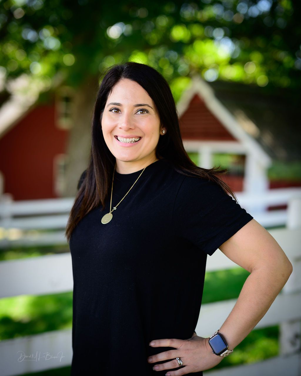 A woman in a black shirt is standing with her hands on her hips in front of a red barn.