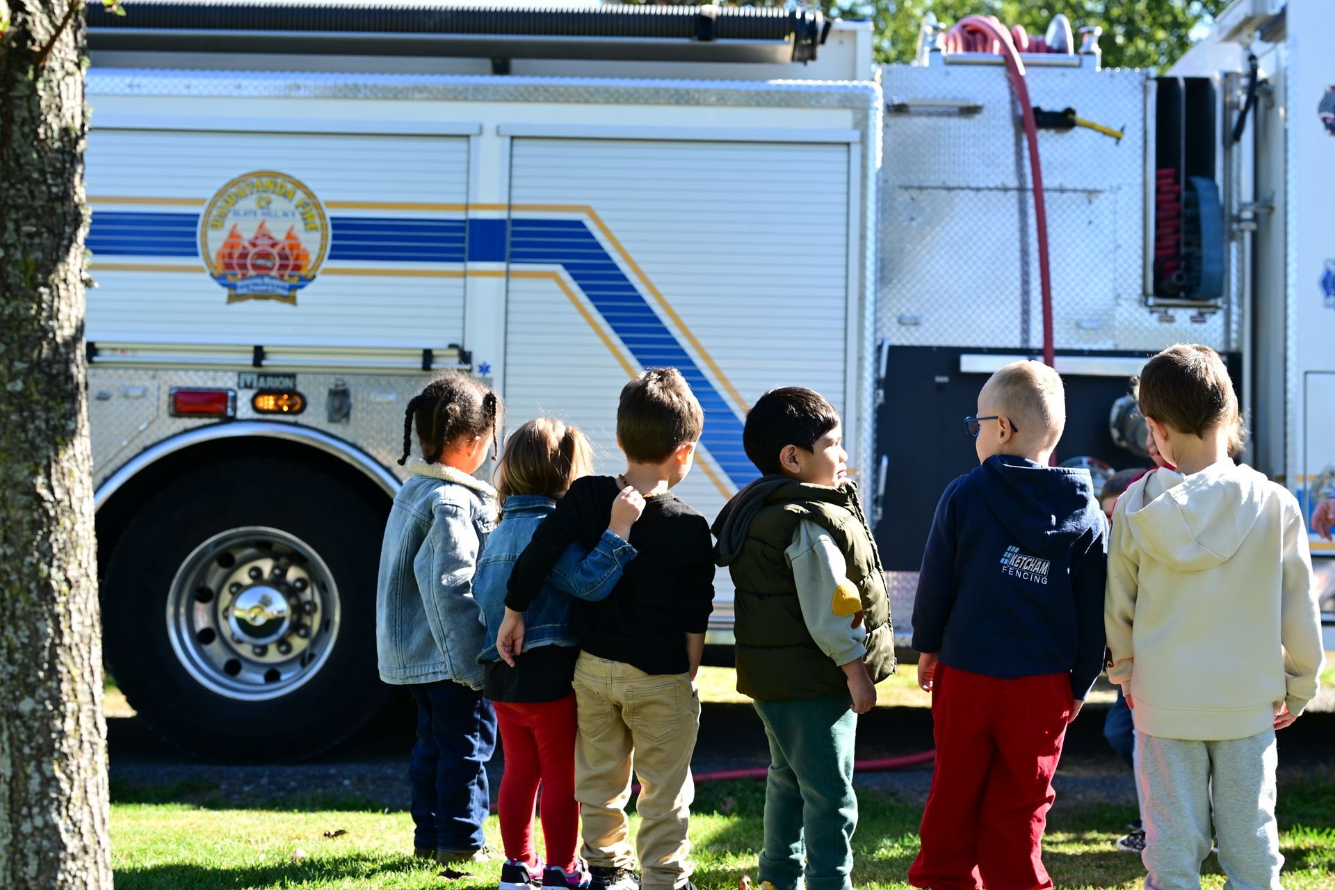Children looking at a fire truck. They're in a line, on a sunny day.