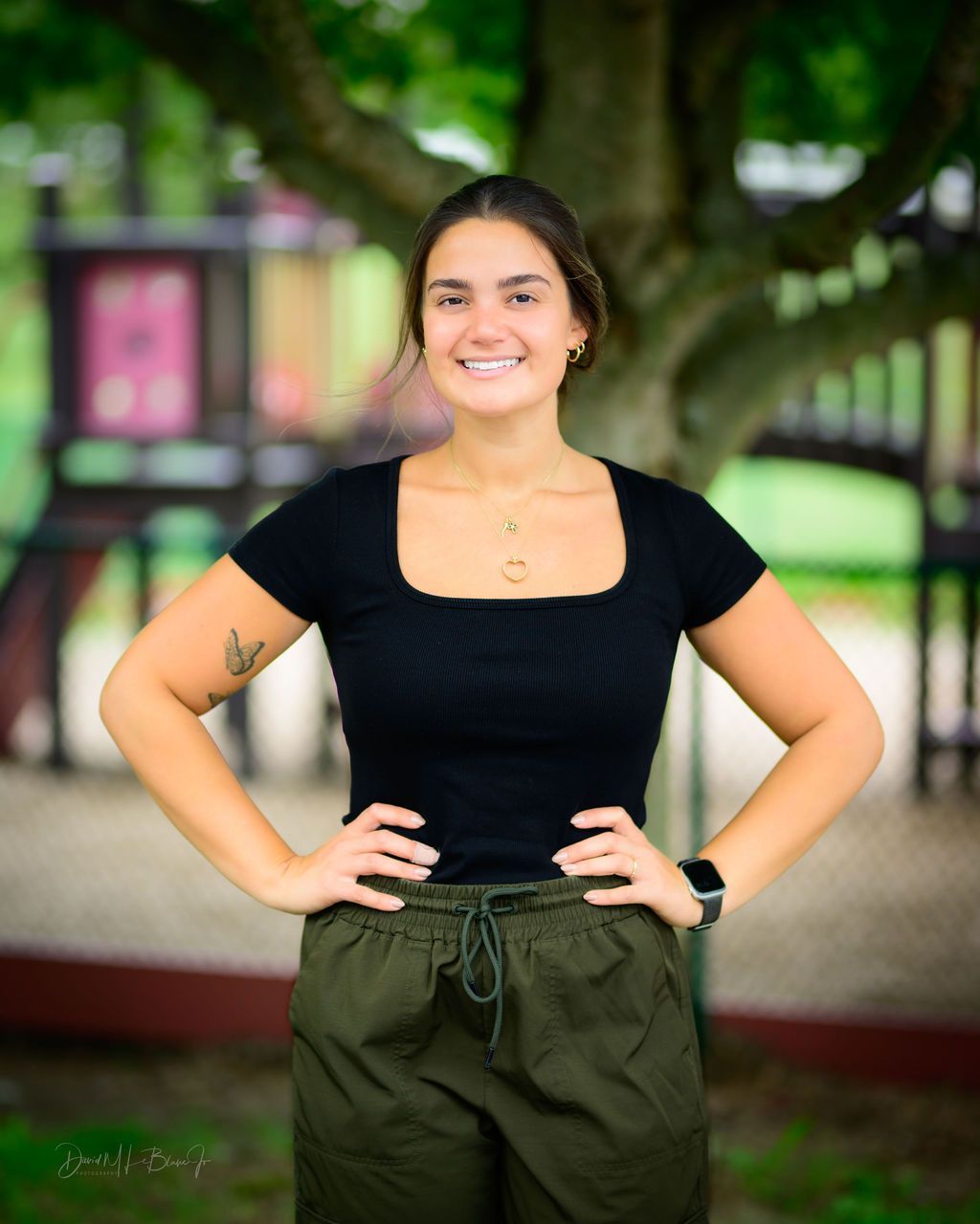 A woman in a black shirt and green pants is standing with her hands on her hips.