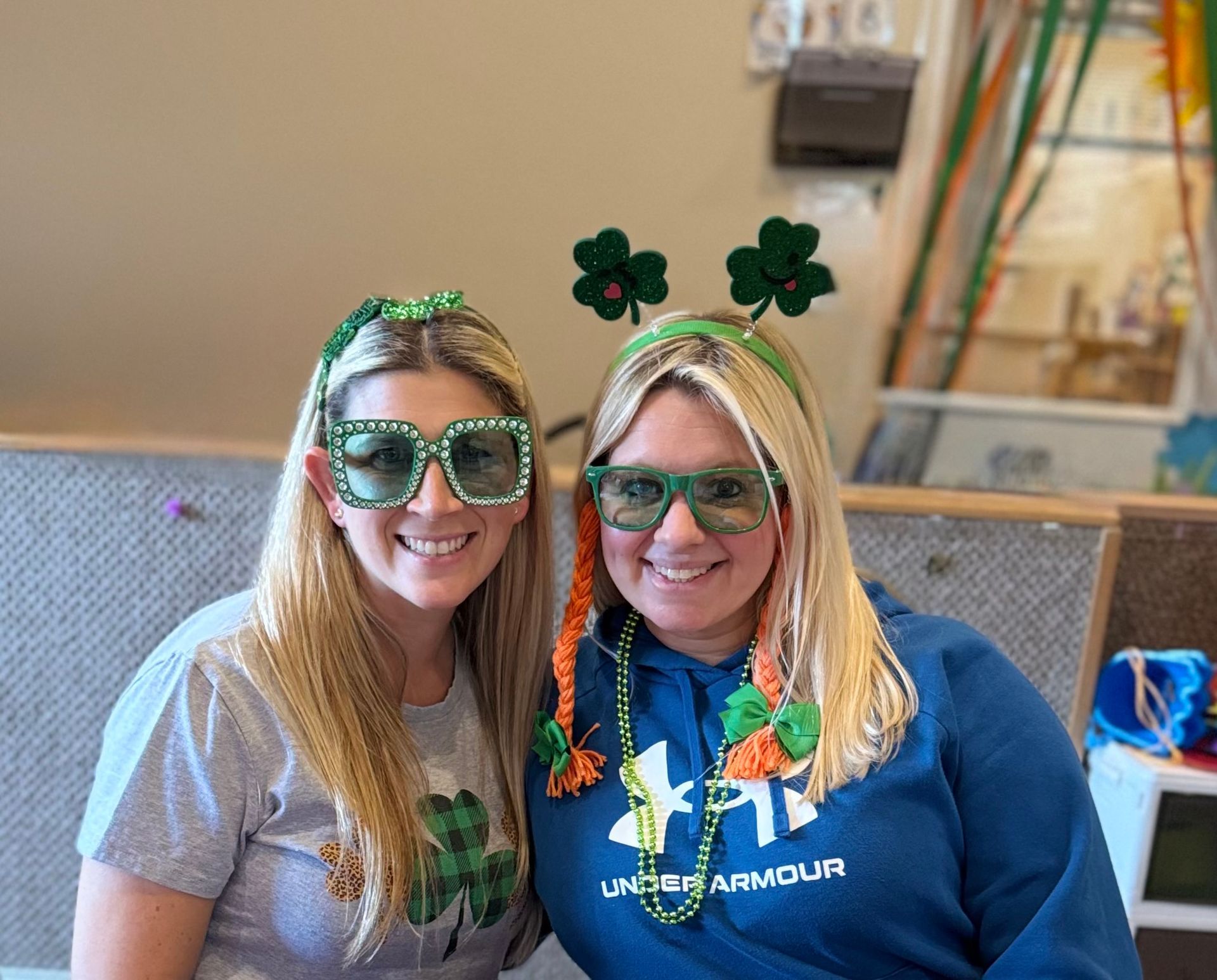 Two women smiling, wearing St. Patrick's Day headbands and green glasses.