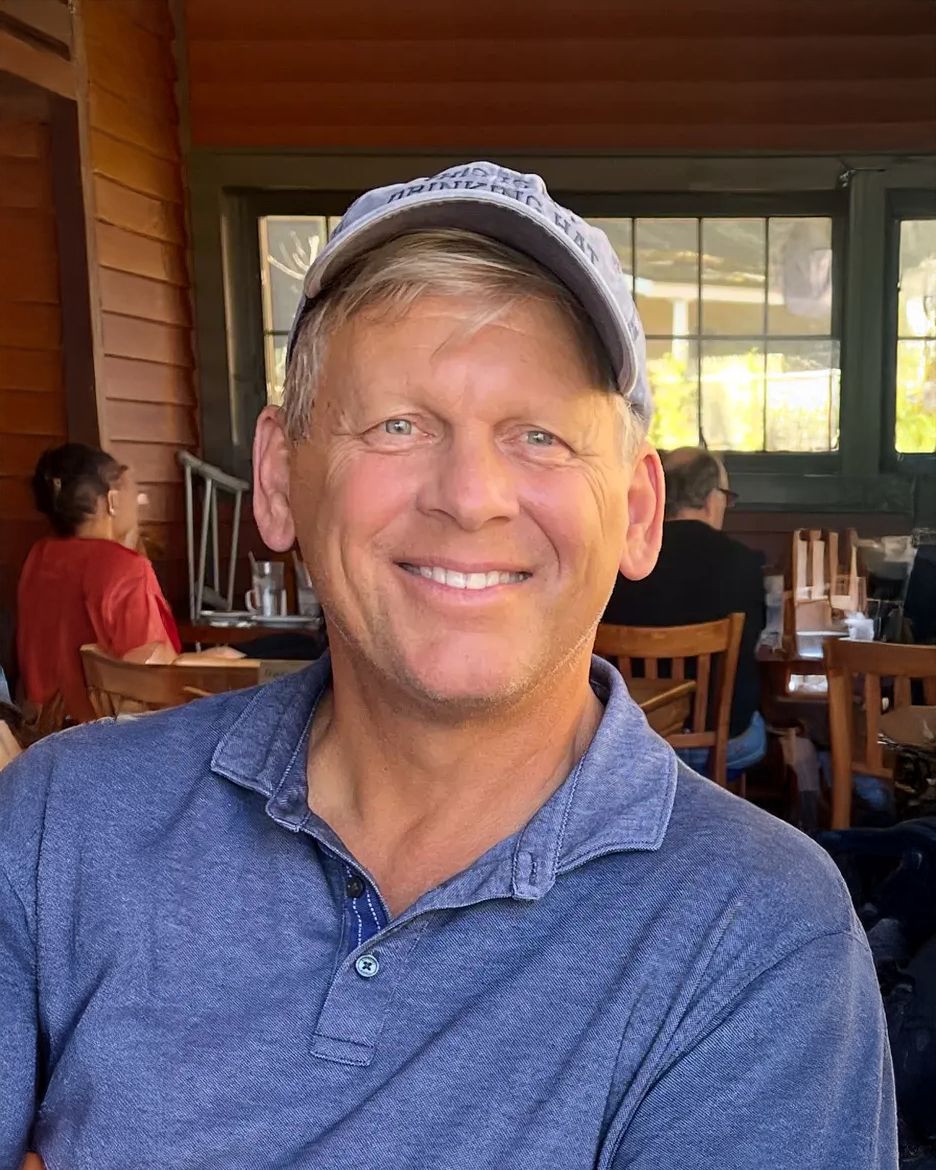A man wearing a hat and a blue shirt is smiling in a restaurant.