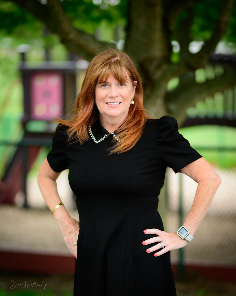 A woman in a black dress is standing in a park with her hands on her hips.