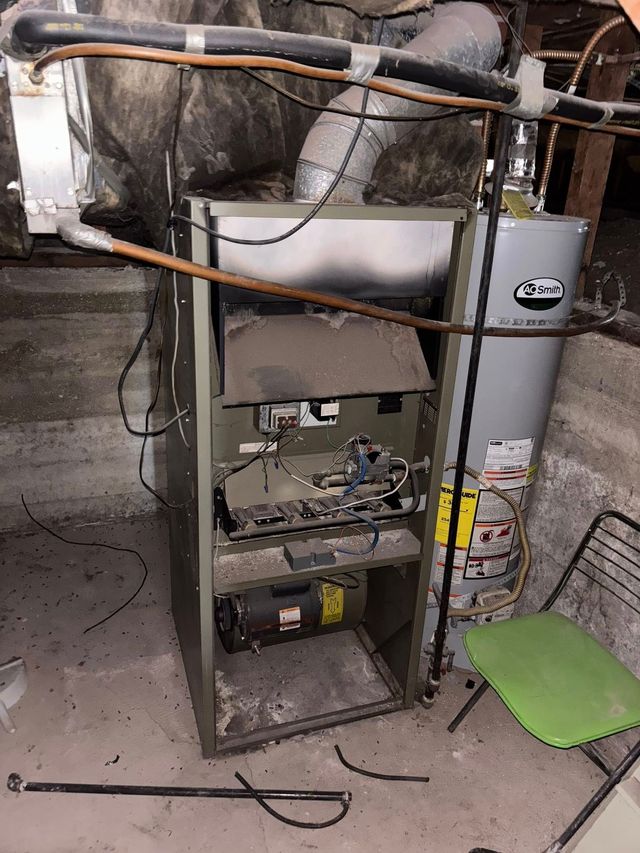 Furnace and water heater in a basement. Furnace is open and dusty. A green chair sits nearby.
