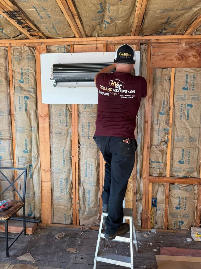 Person on a stepladder installs electrical panel on a wall. The wall is framed and insulated.