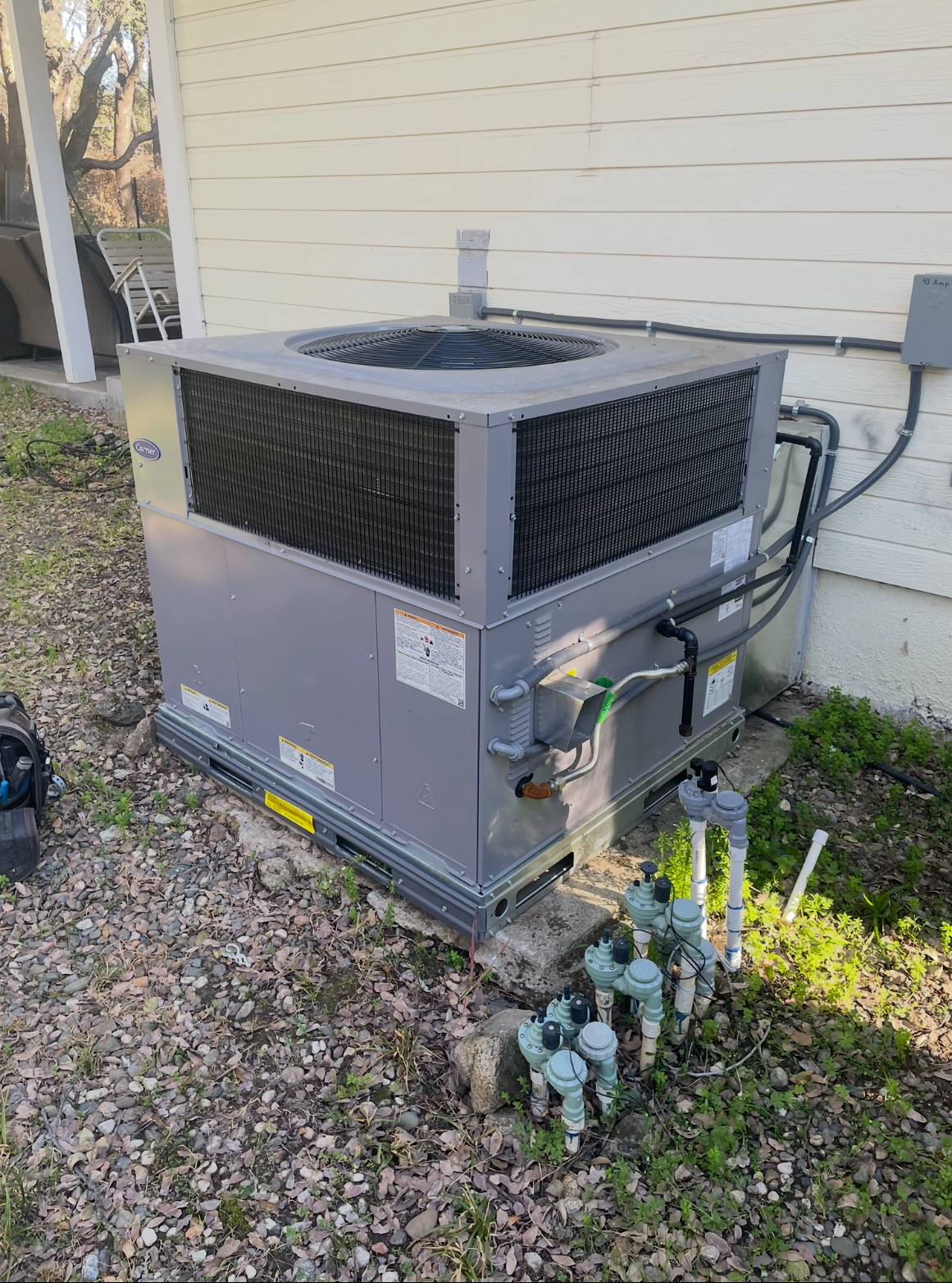 Gray Carrier air conditioning unit outside a white building on gravel.