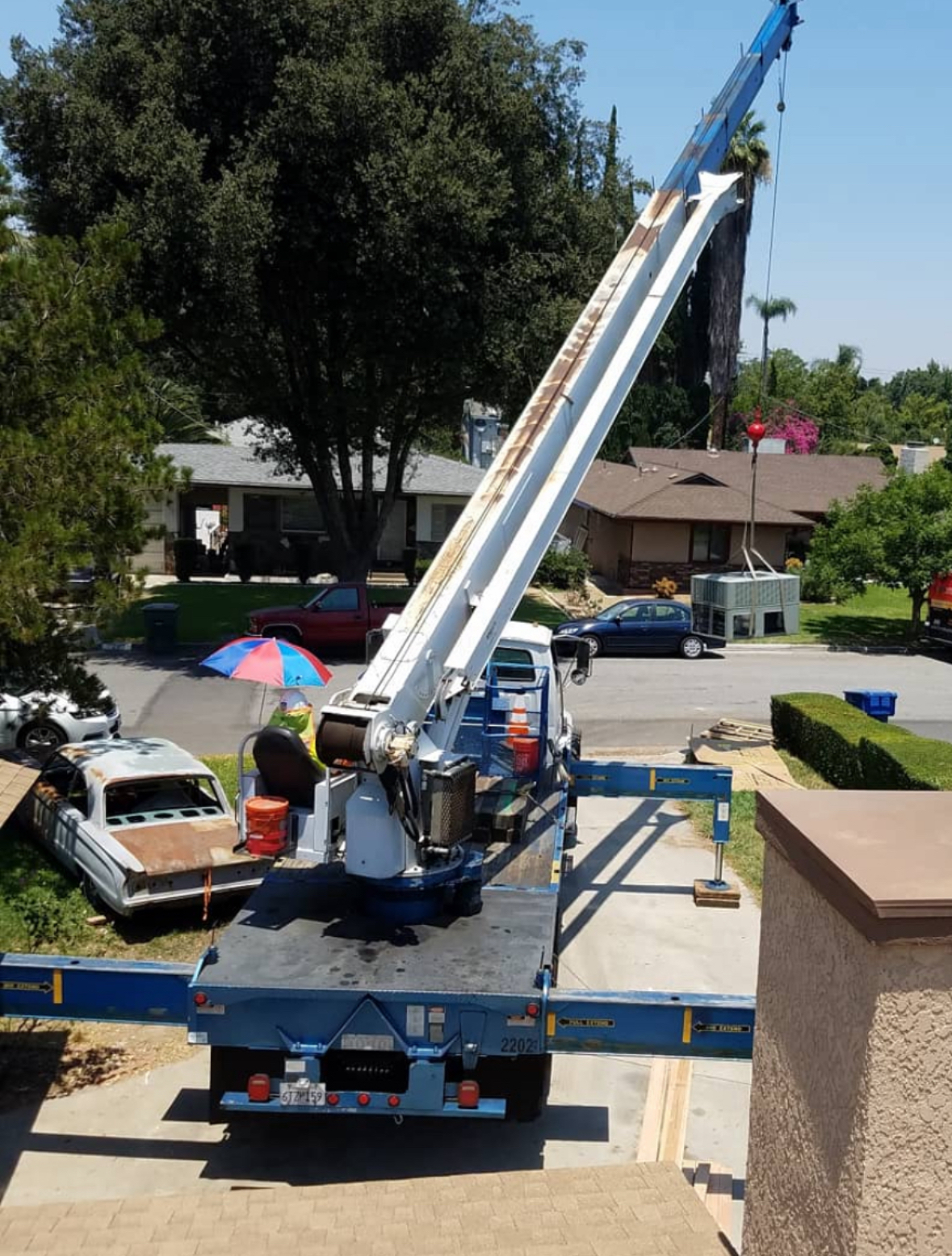 Truck with crane lifting equipment in residential area. Blue truck, sunny day.