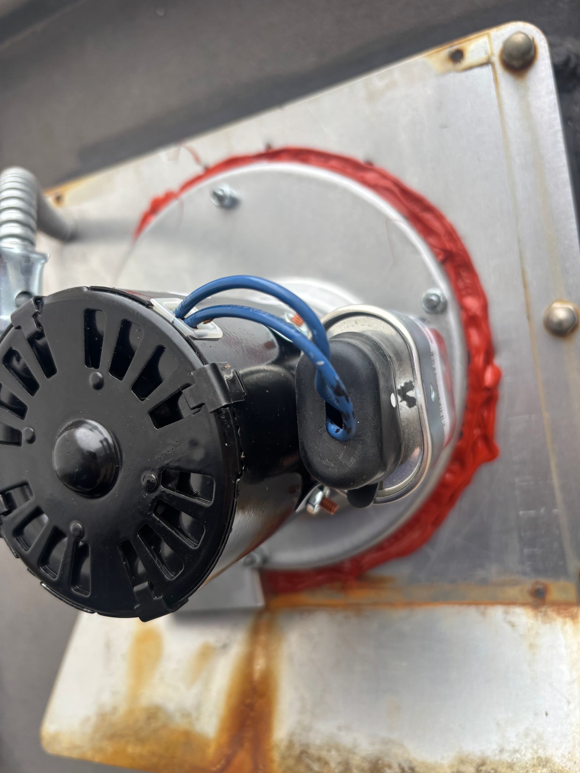 Close-up of a motor with a circular metal plate, red sealant, and blue wires. Rusty surface visible.