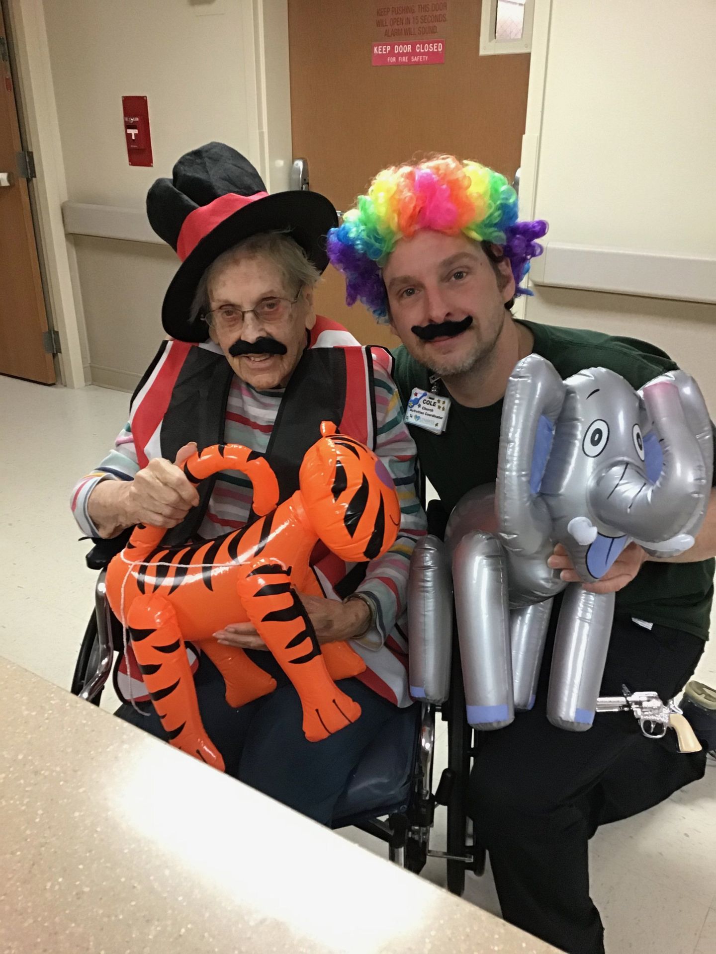 Elder posing with staff member wearing hats and holding balloon animals at Lenawee Medical Care Facility in Adrian, MI