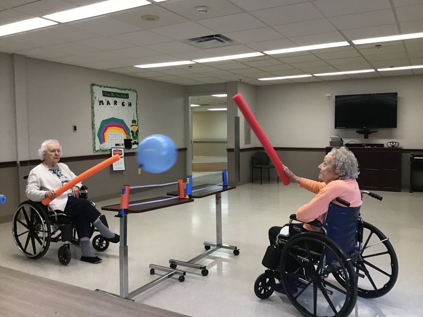 Two Elders playing tennis with pool noodles and a balloon at Lenawee Medical Care Facility in Adrian, MI