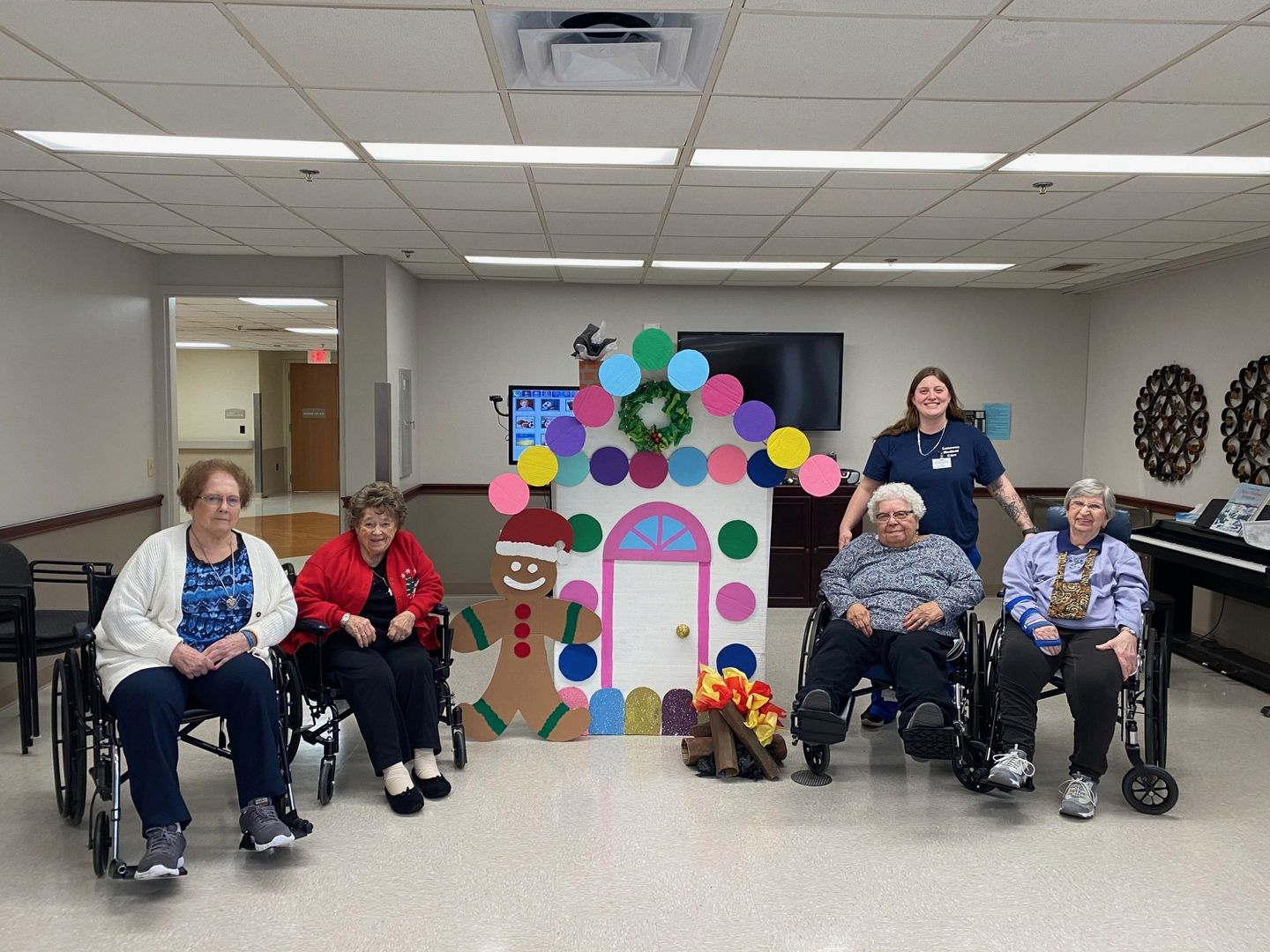 Elders and staff member posing next to ginger bread house display at Lenawee Medical Care Facility in Adrian, MI
