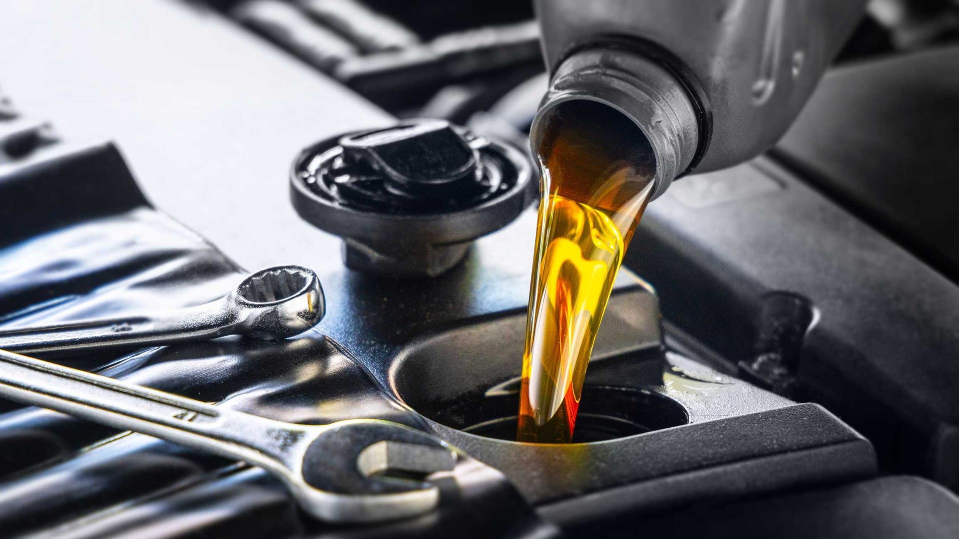 Pouring oil into a car engine, with wrenches and an oil cap visible.