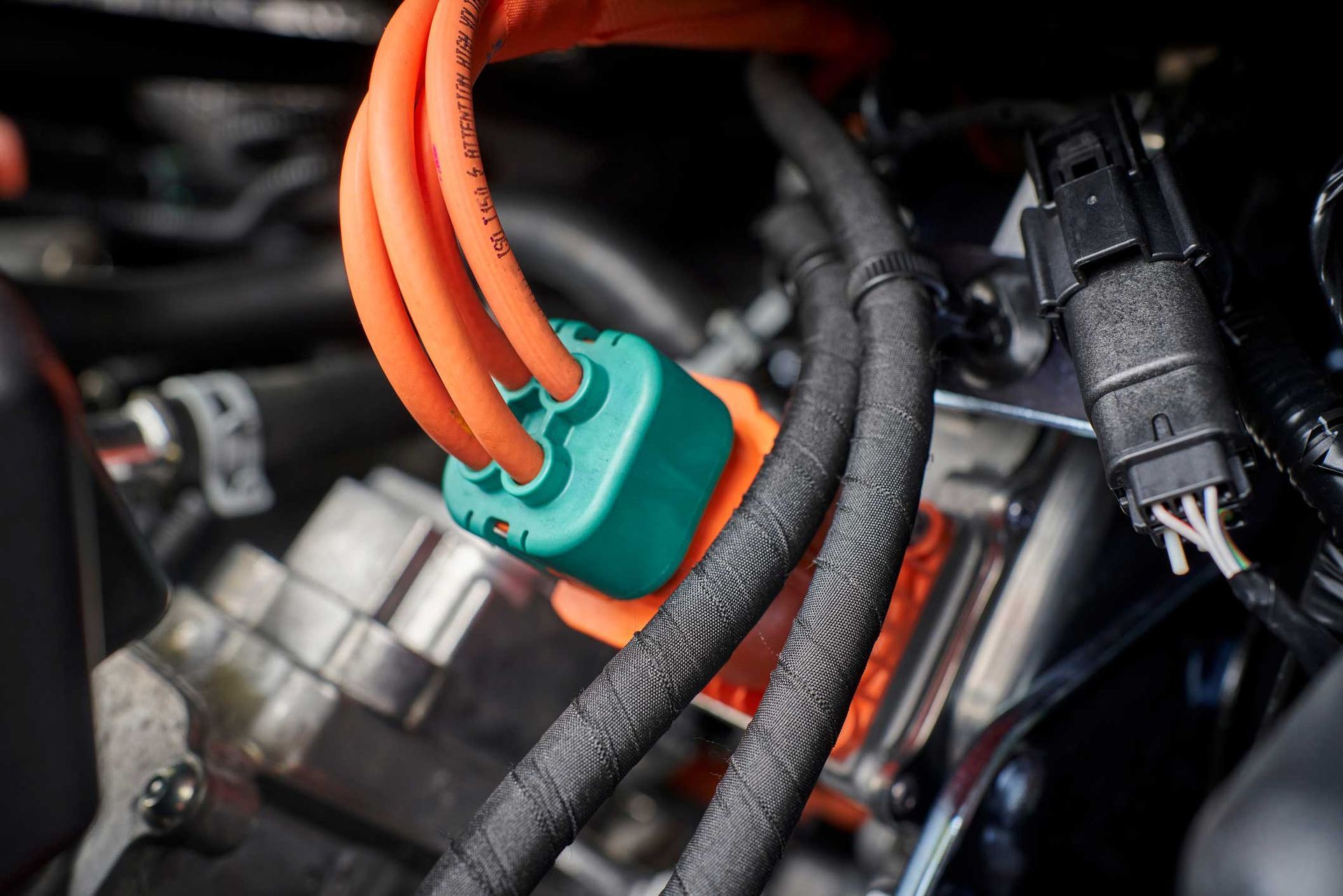 Orange and black EV wiring with green connector, inside a vehicle engine compartment.