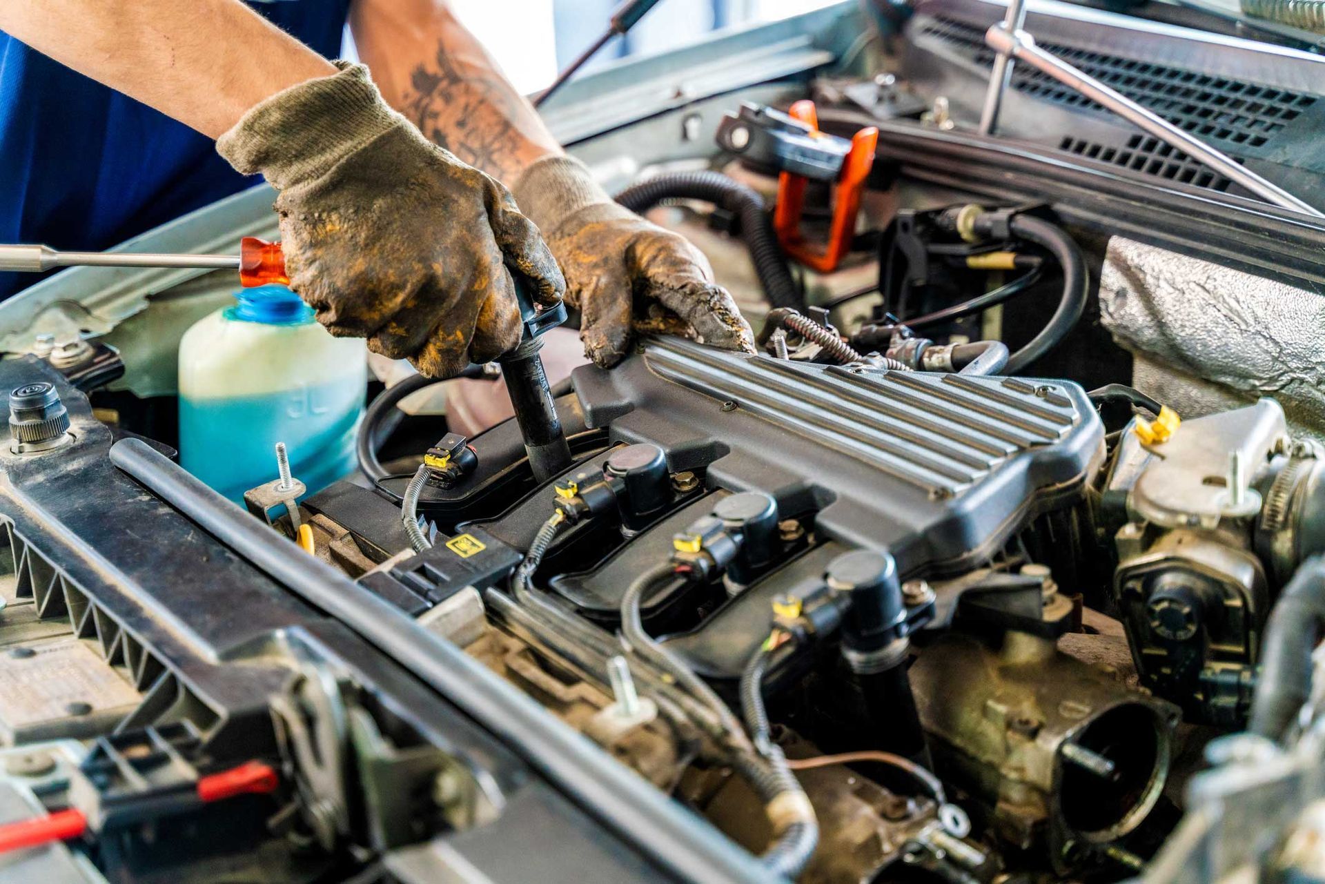 Mechanic working on a car engine with gloved hands in a brightly lit setting.