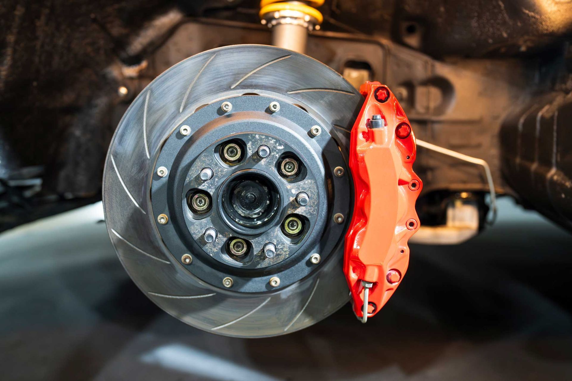 Car brake disc with red caliper, showing slotted rotor and bolts.