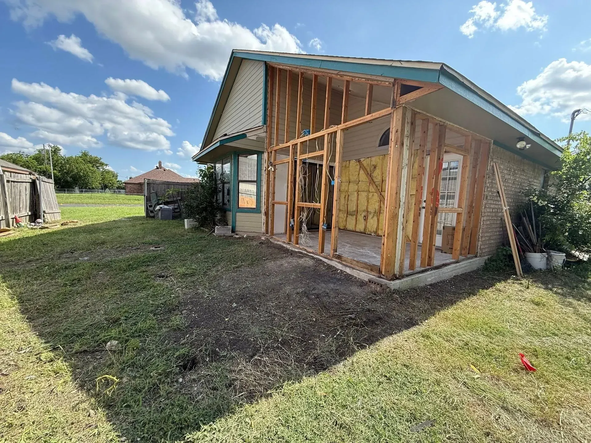 Exterior of a house under construction, exposed wooden framing, green grass, blue sky.