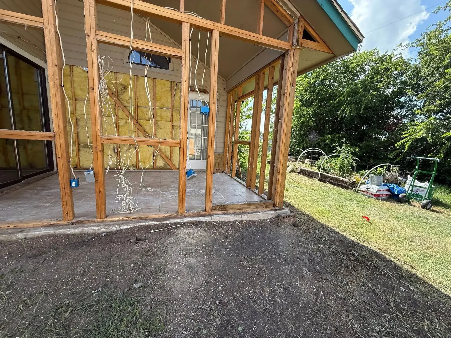 Exterior wall framing partially stripped, exposing insulation and wires; yard with green grass.
