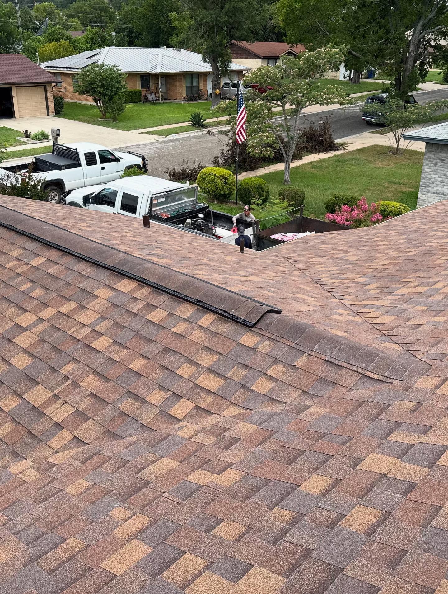 View of residential rooftops and street; a truck and workers on roof.