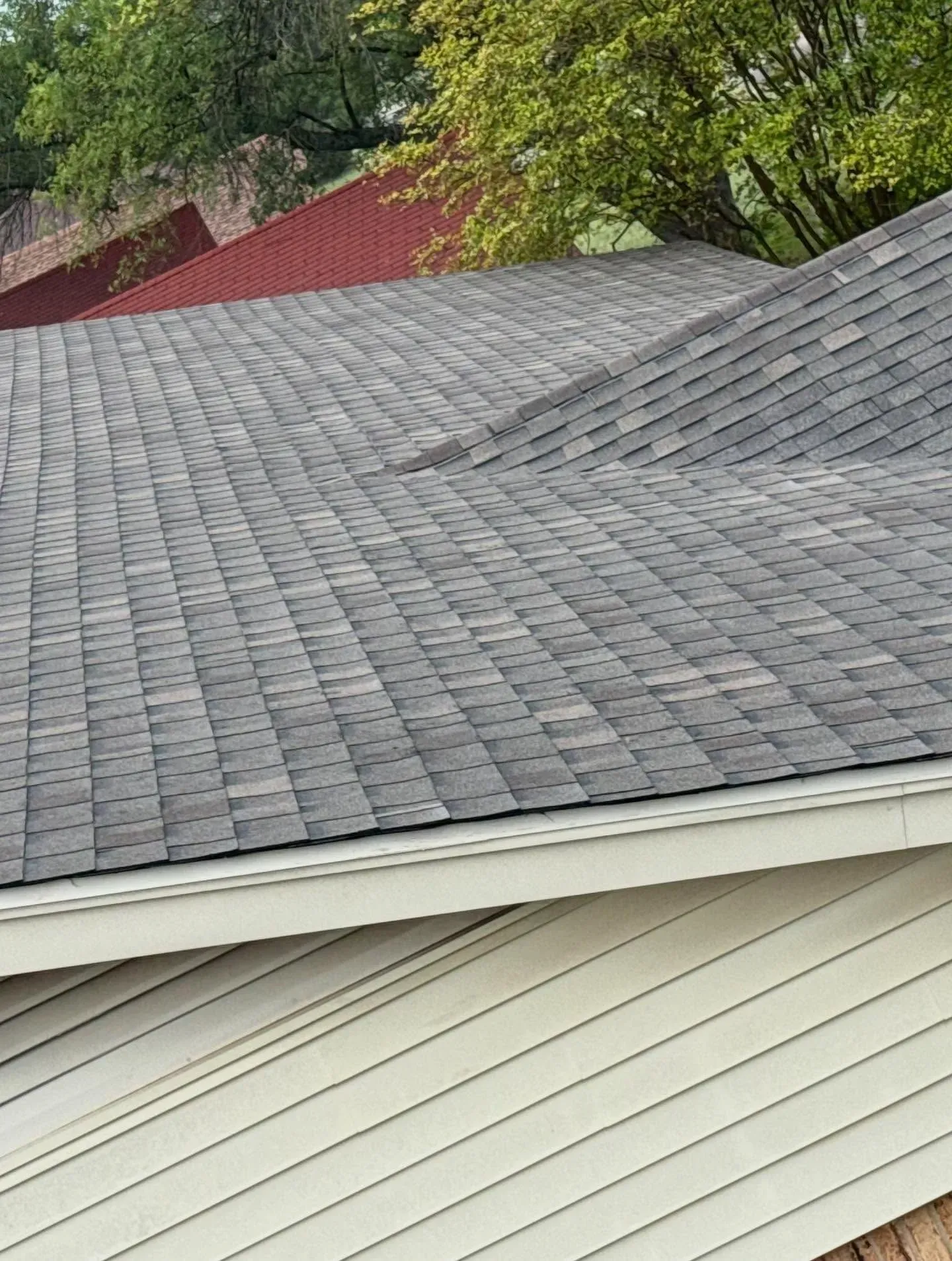 Gray and brown shingled roof with white trim; red roof in the background, trees above.