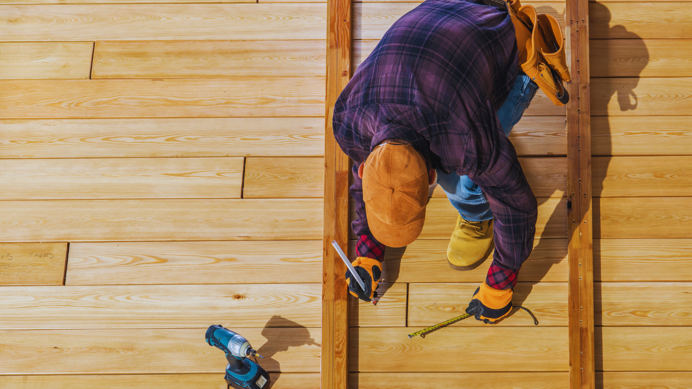 Carpenter installing wooden siding, using a measuring tape and pencil.