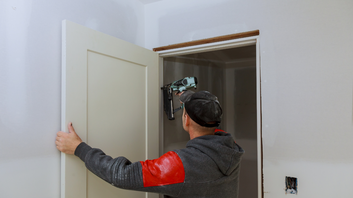 Man installing a door in a new home. He is using a nail gun.