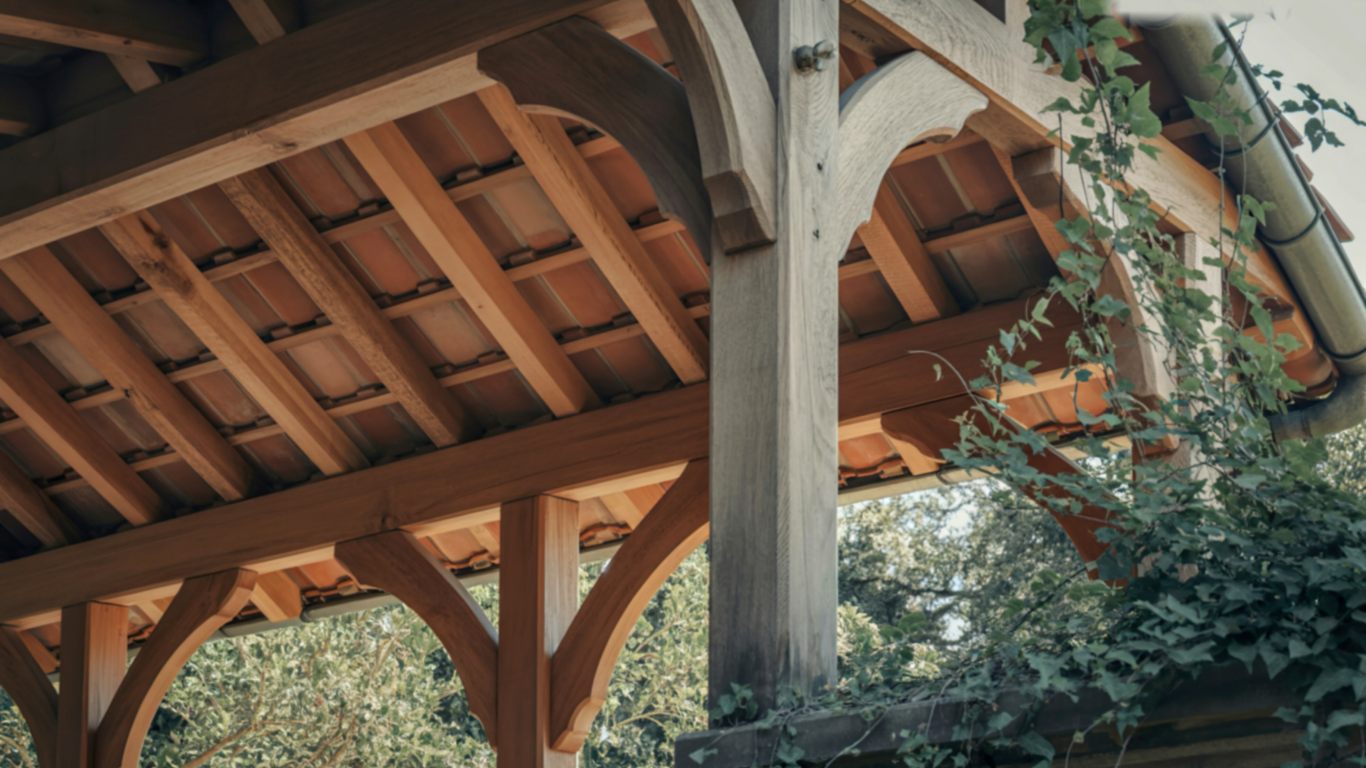 Wooden pergola with tiled roof, supported by posts. Green vines grow nearby.