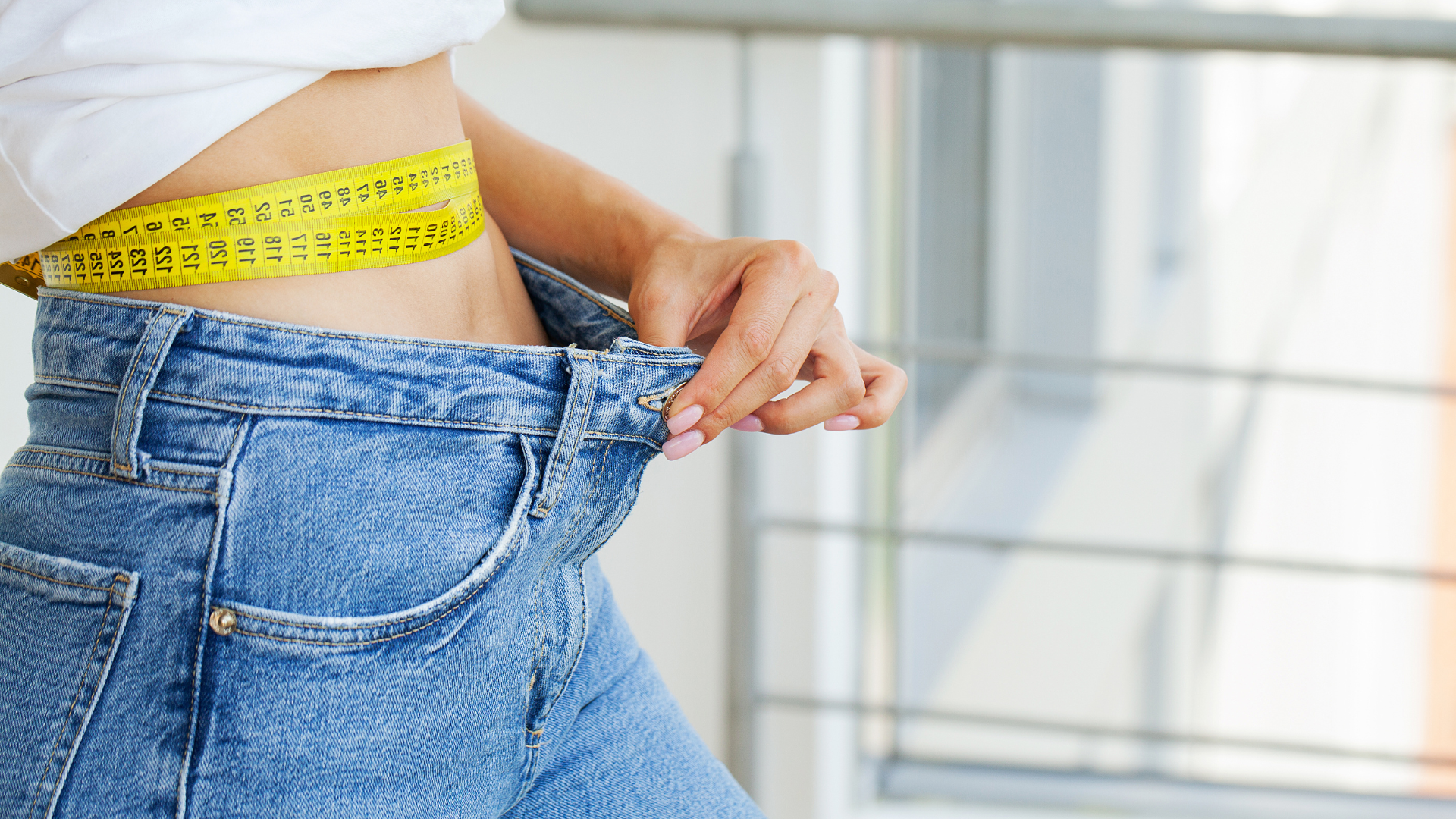 A woman is measuring her waist with a tape measure.